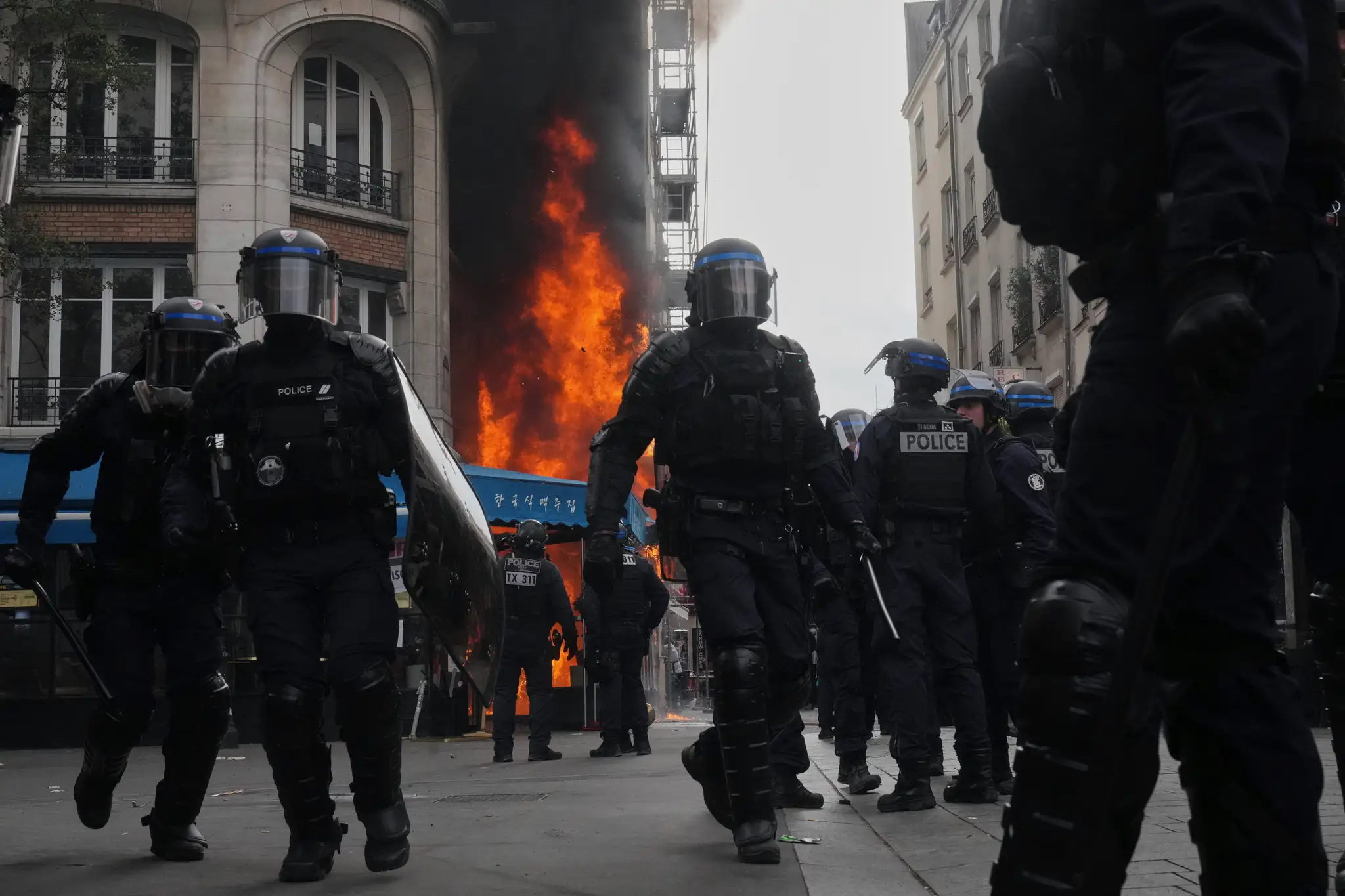 Policajní ťažkoodenci zaujímajú pozície pred horiacou reštauráciou počas protestnej akcie v Paríži.
