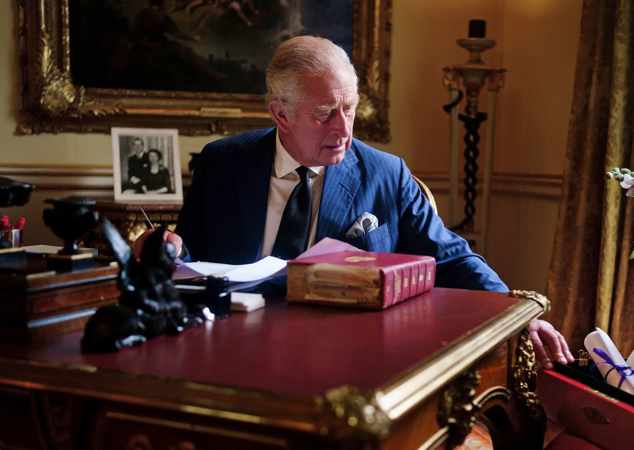 Nový britský kráľ Karol III. sedí za pracovným stolom a vyberá z oficiálnej červenej krabice korešpondenciu.