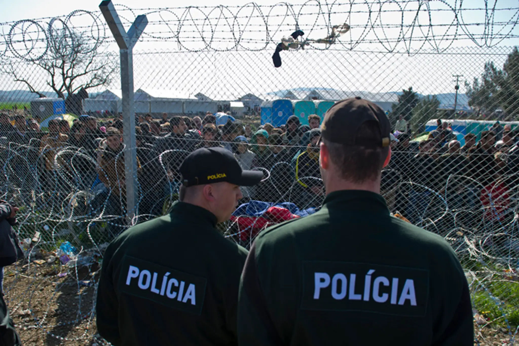 Na snímke migranti na gréckej strane hranice a slovenskí policajti. 