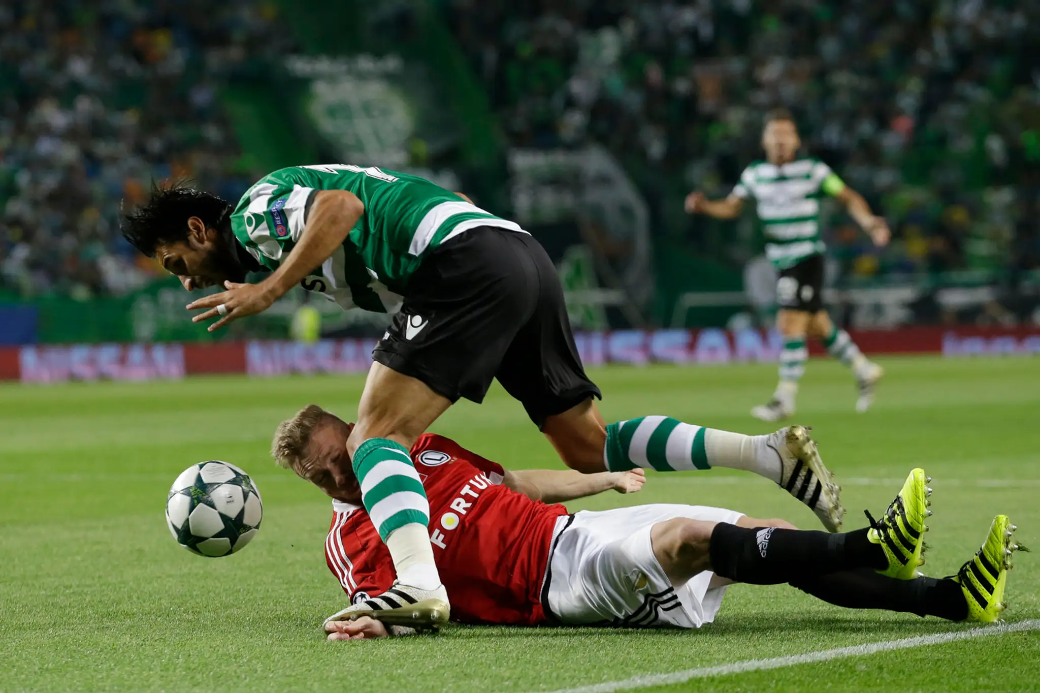 V ostrom súboji na zemi hráč Legie Varšava Jakub Rzezniczak a Bryan Ruiz zo Sportingu Lisabon v dueli LM.