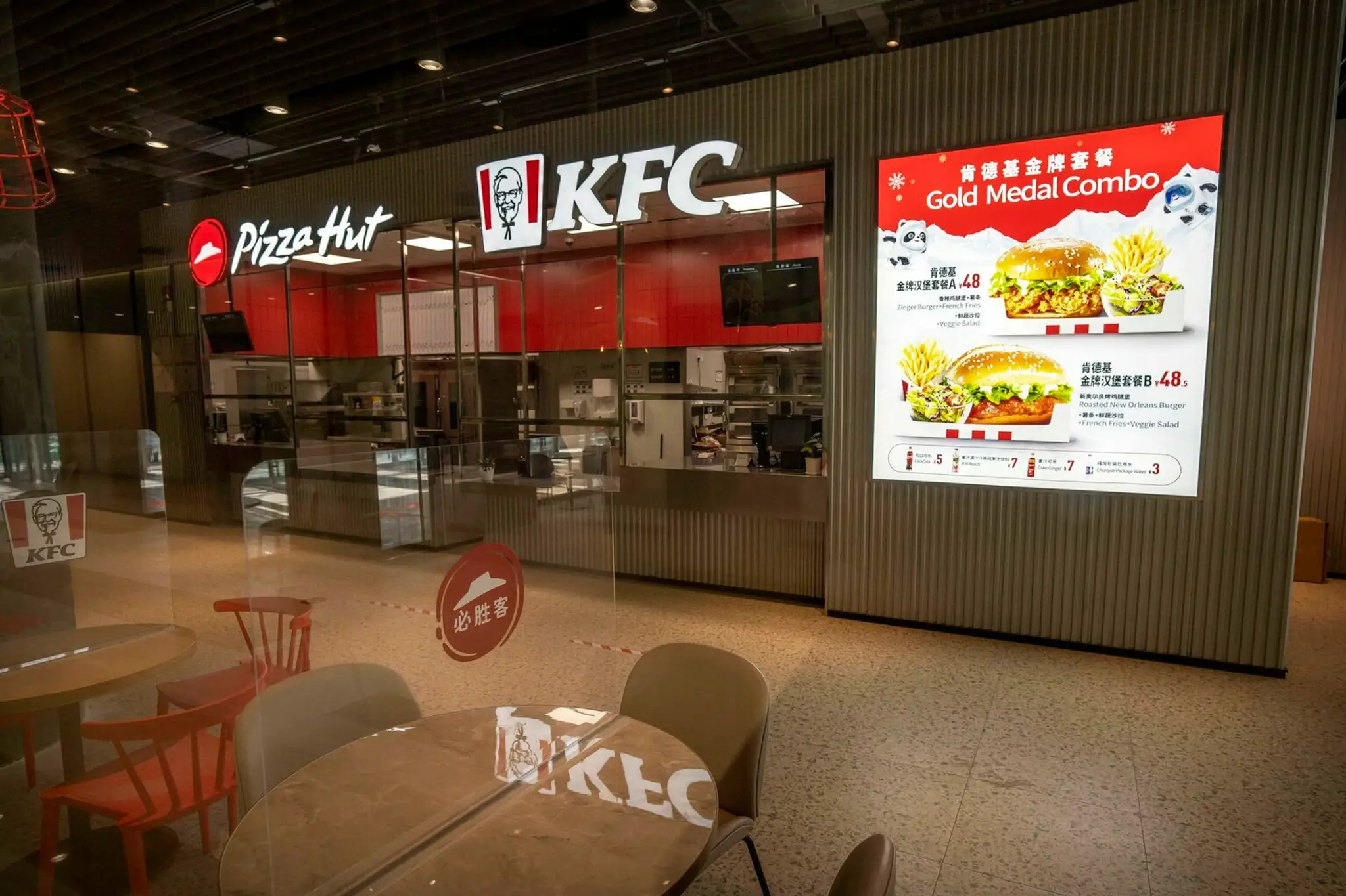 Priečky z plexiskla oddeľujú miesta na sedenie v reštauráciách s rýchlym občerstvením Pizza Hut a KFC v olympijskej dedine.