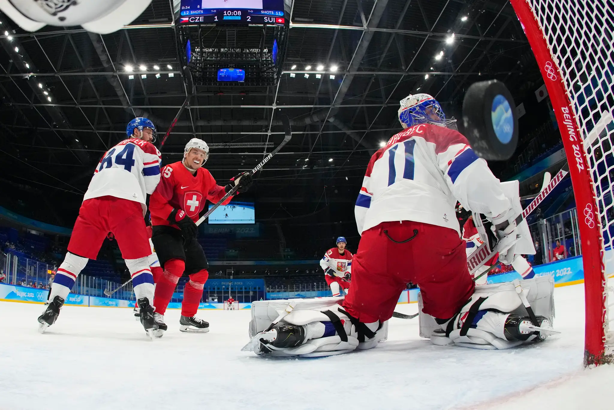 Švajčiar Sven Andrighetto sleduje strelu spoluhráča, ktorá končí za českým brankárom v zápase ZOH 2022.