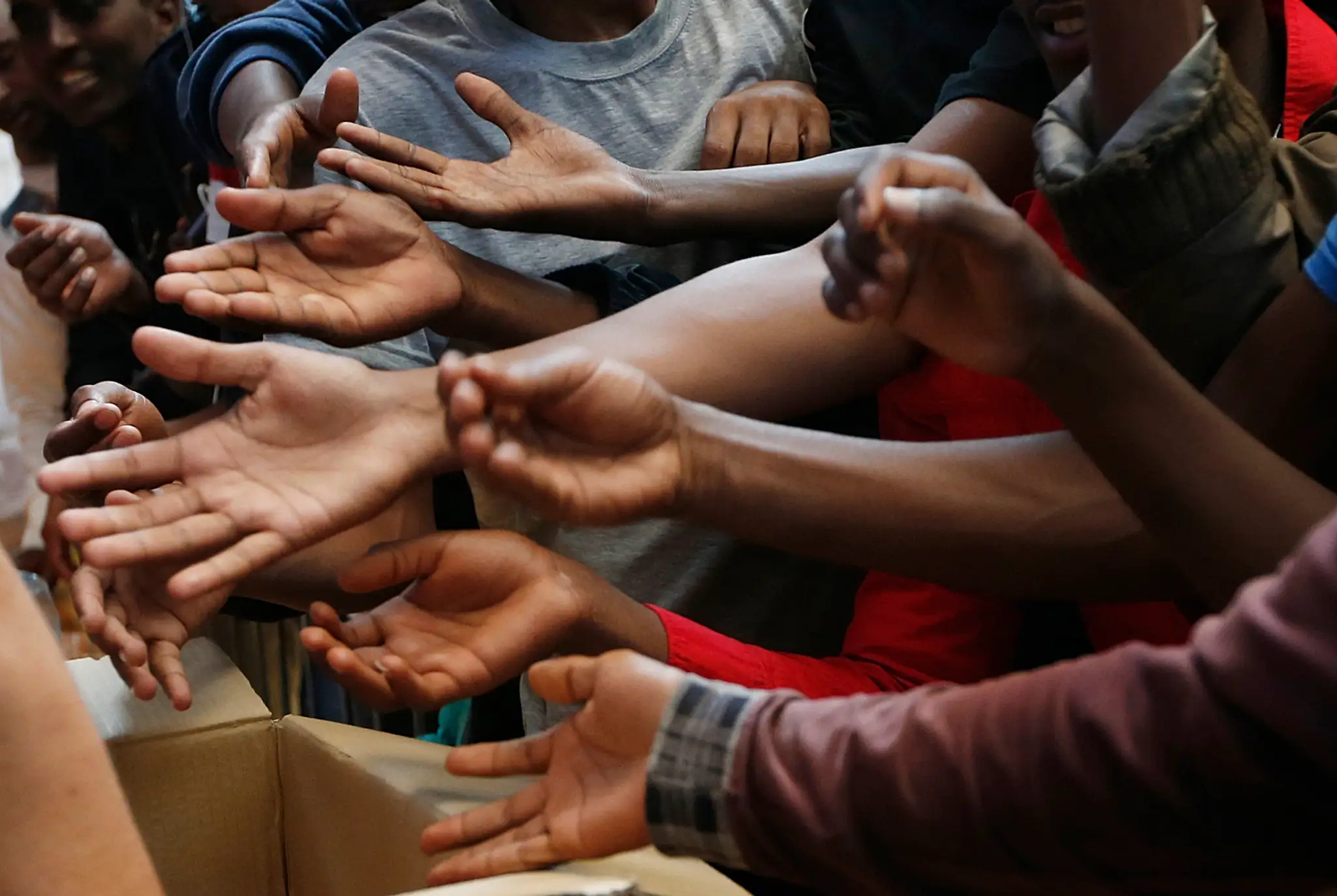 Migranti naťahujú ruky na centrálnej milánskej železničnej stanici, aby dostali jedlo. 11. jún