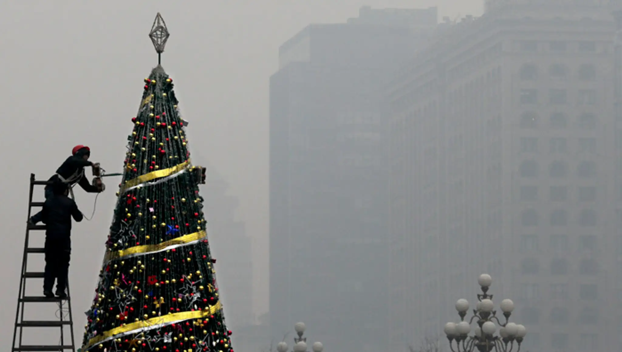 Zamestnanec zdobí vianočný stromček pred nákupným centrom počas smogovej pohotovosti v Pekingu.