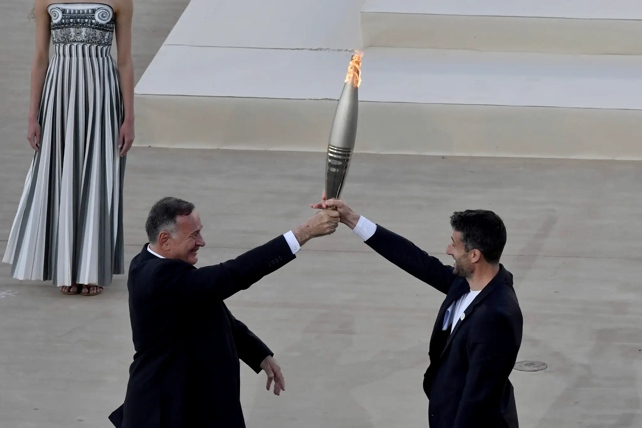 Šéf Gréckeho olympijského výboru Spyros Capralos (vľavo) odovzdáva olympijský oheň predsedovi francúzskeho organizačného výboru Tonymu Estanguetovi.
