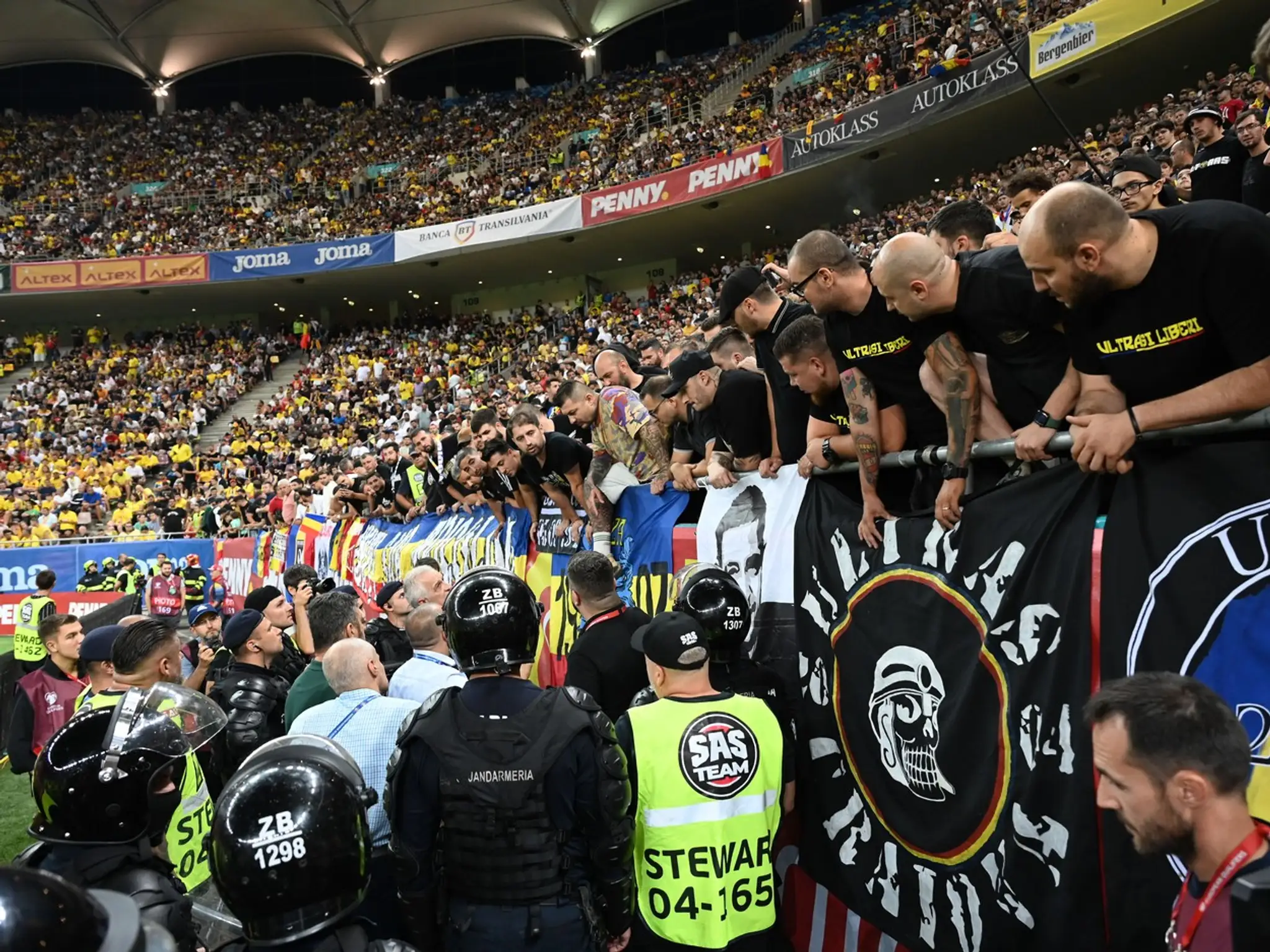 Policajti stoja pod tribúnou, na ktorej stoja ultras.