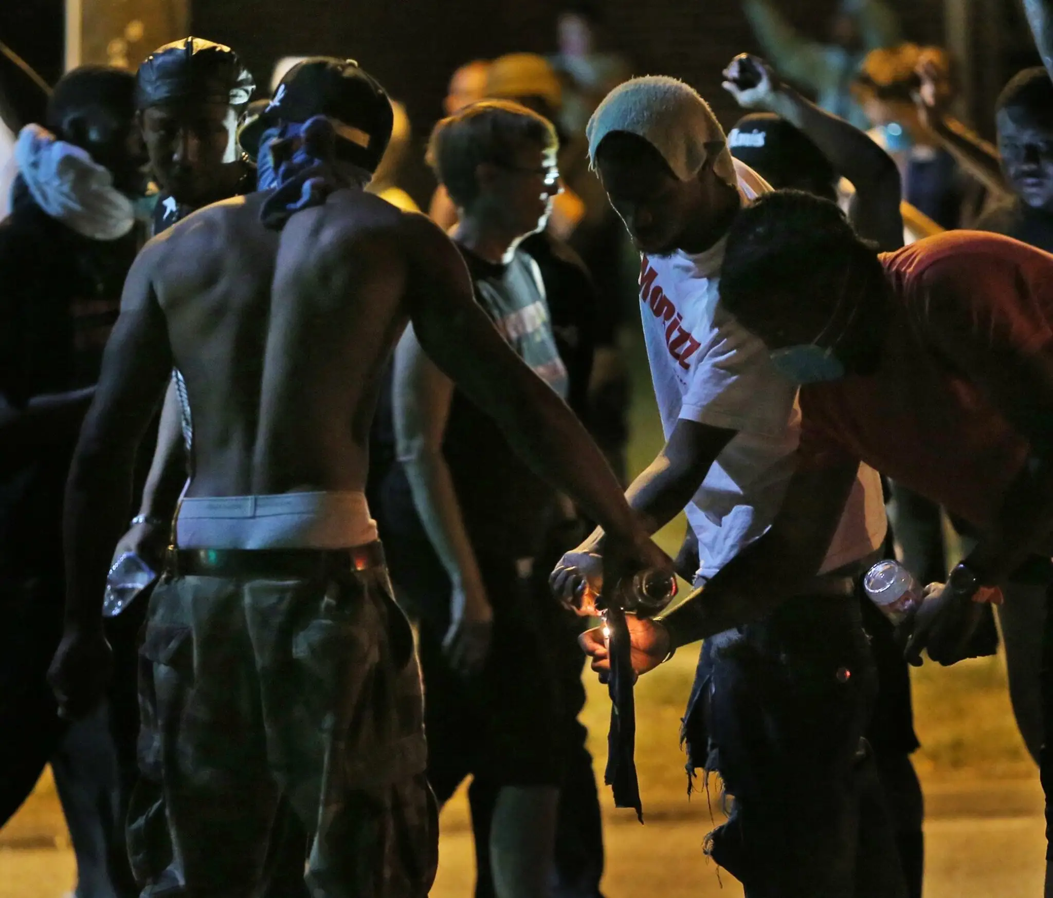 Maskovaní rasovo motivovaní demonštranti si pripravujú zápalné fľaše proti policajtom v americkom meste Ferguson.