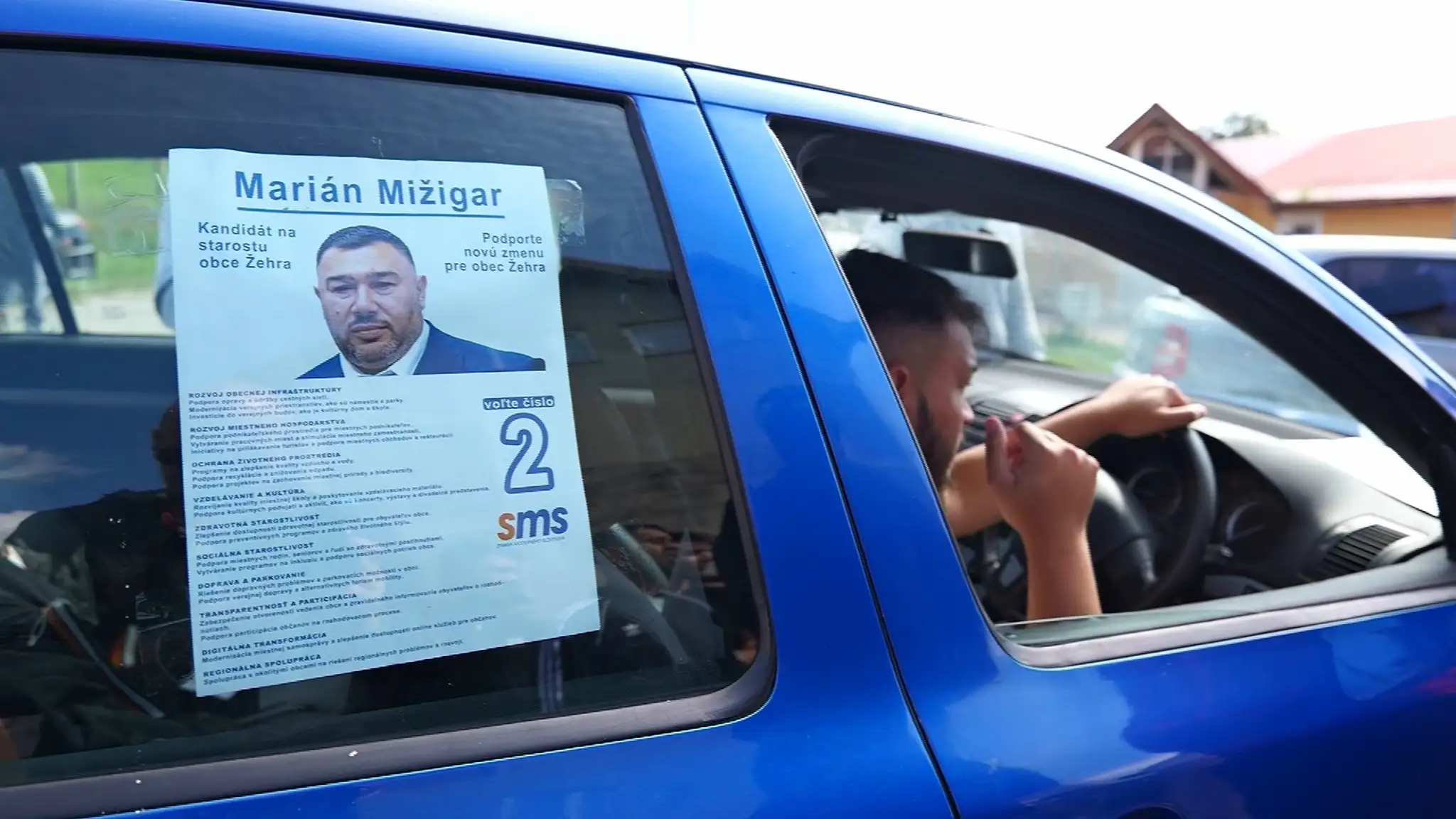 Miestni s plagátom s podobizňou kandidáta.