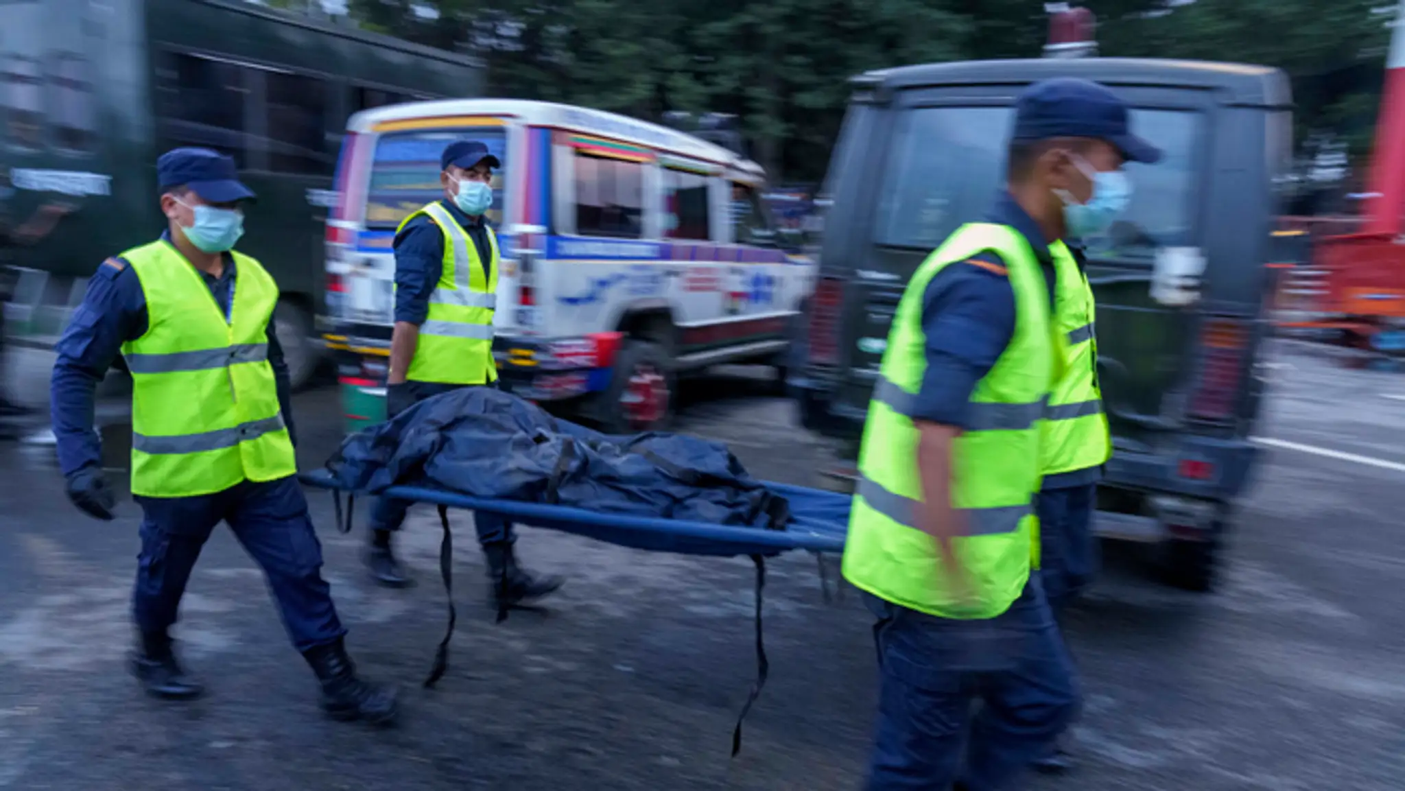Nepálski policajti prenášajú telo obete leteckého nešťastia do sanitky.