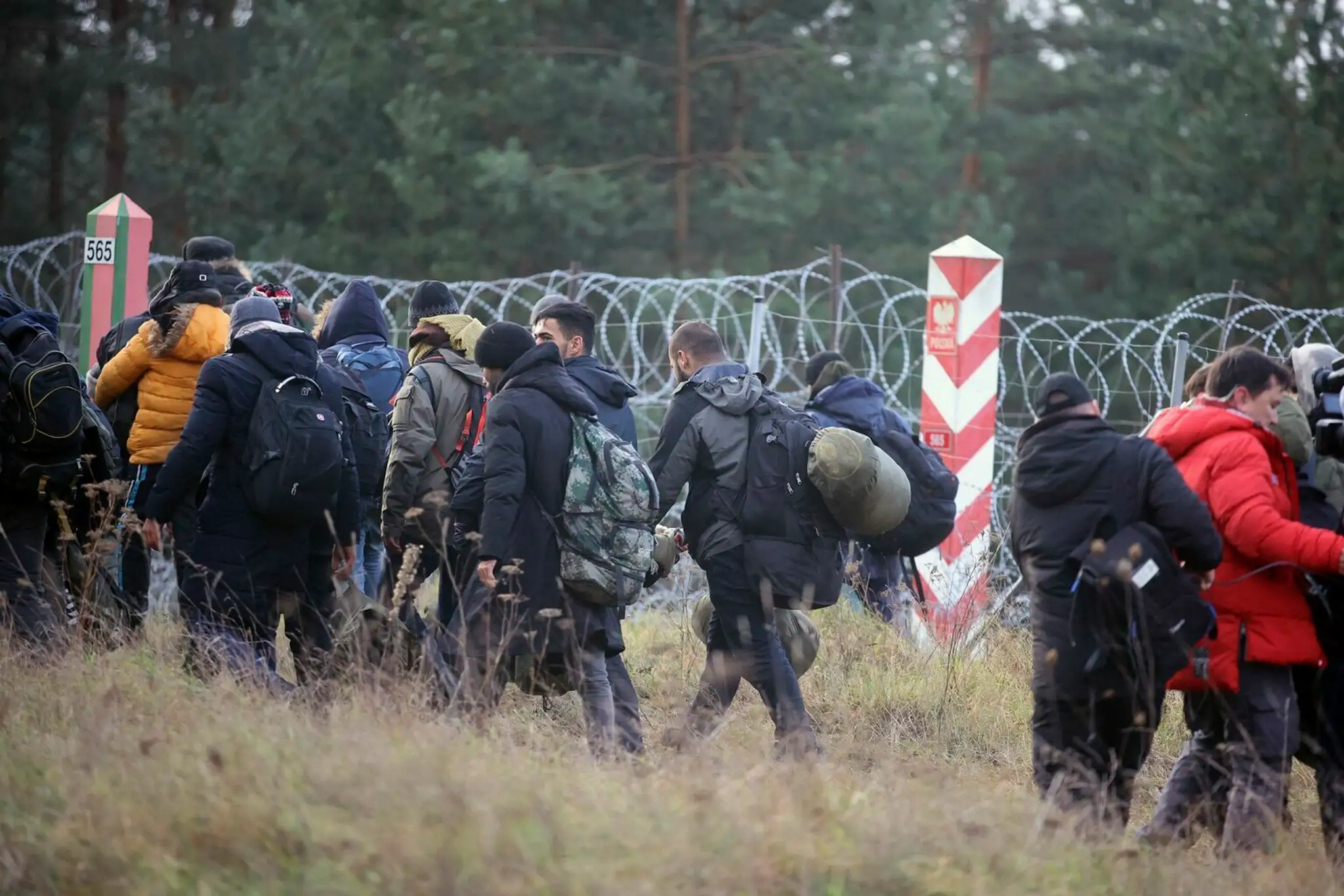 Migranti z Blízkeho východu a iných krajín kráčajú pozdĺž oplotenia s ostnatým drôtom na hranici pri bieloruskej dedine Grodno.