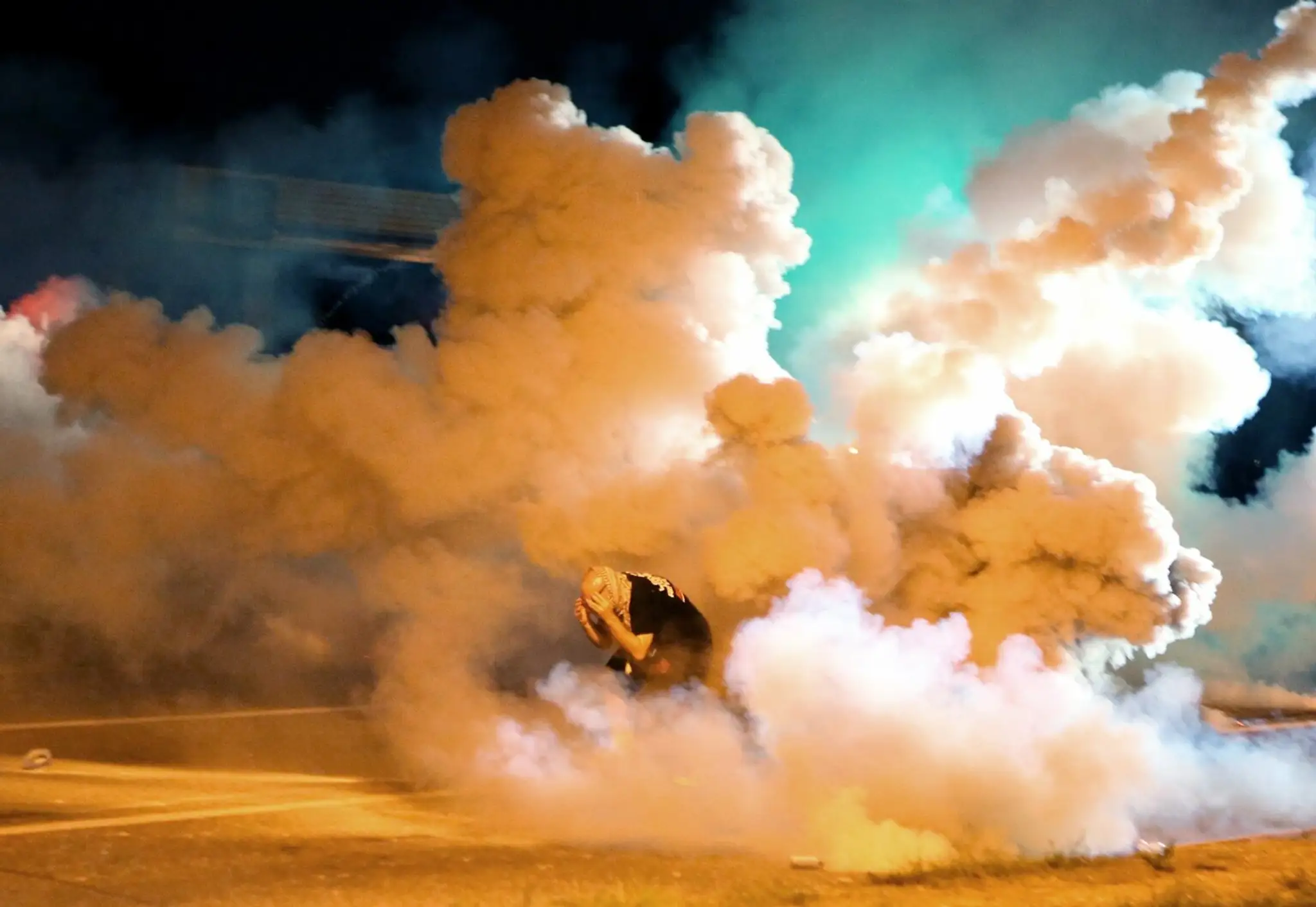Demonštrant uteká pred slzotvorným dymom pri zásahu polície v americkom meste Ferguson.