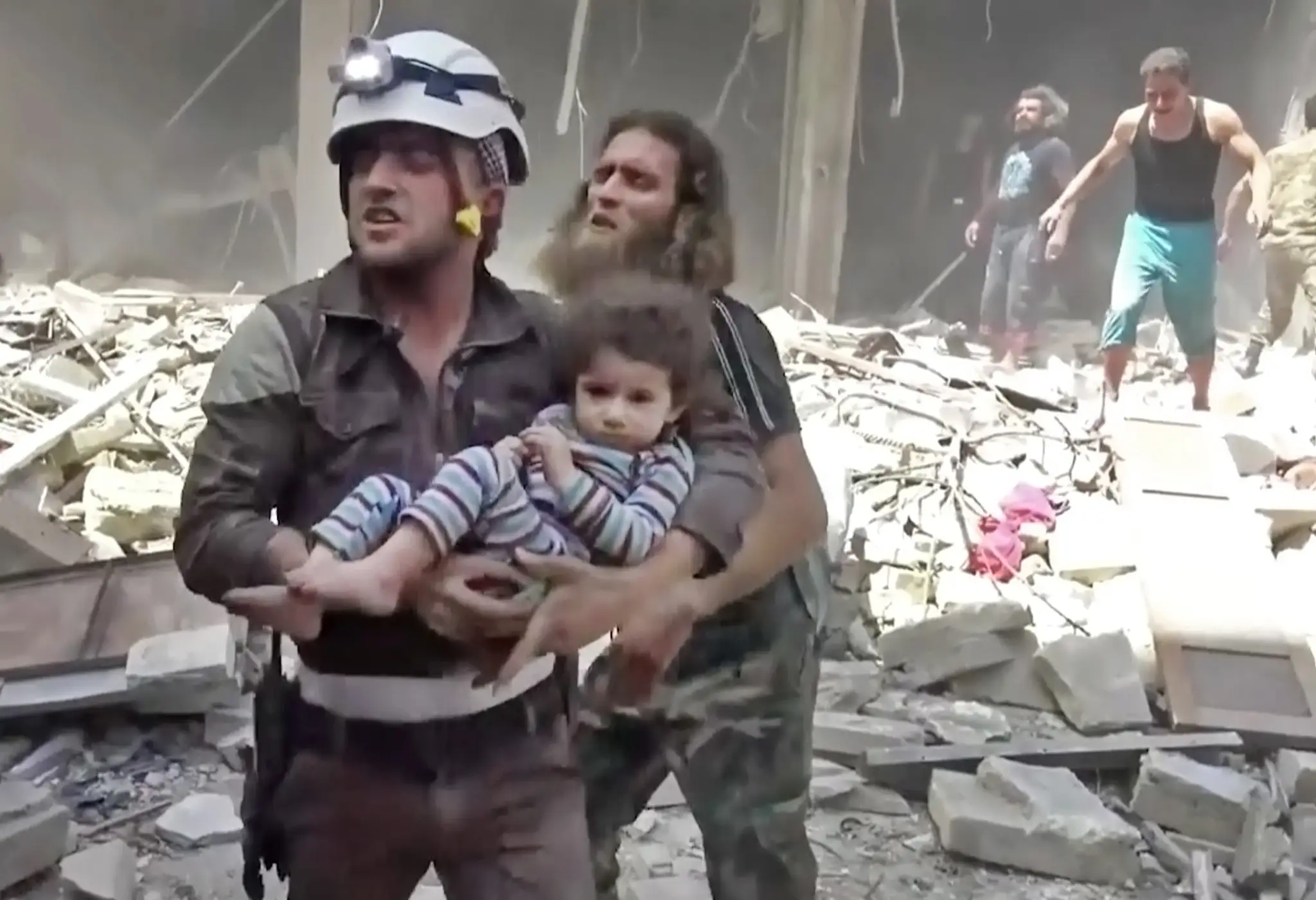 Na snímke miestny člen civilnej obrany Biele helmy nesie dieťa po náletoch v povstalcami ovládanej časti mesta Aleppo