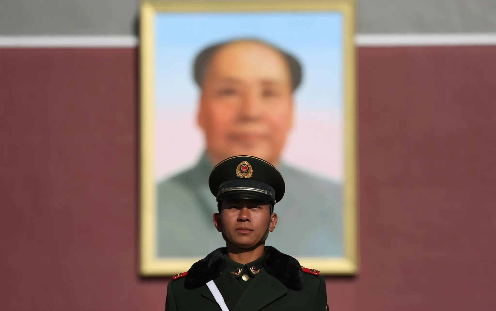 Čínsky policajt stojí pred vchodom do Zakázaného mesta s nadrozmerným obrazom Mao Cetunga v Pekingu.