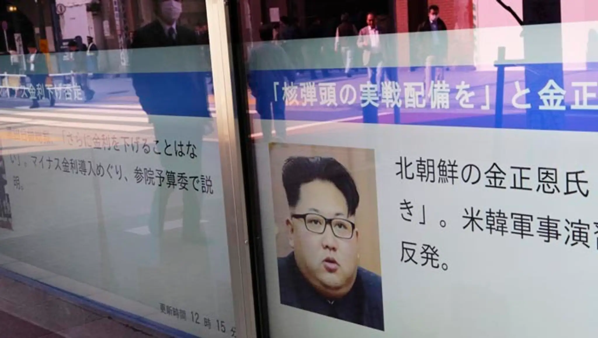 Ľudia v odraze výkladu kráčajú okolo portrétu severokórejského lídra Kim Čong-una v Tokiu.
