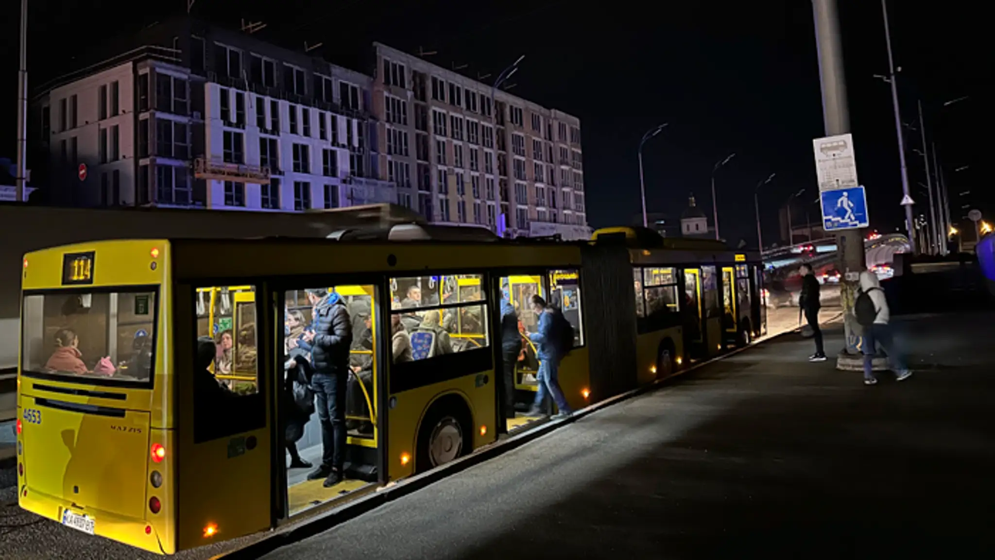 Ľudia nastupujú do autobusu na tmavej ulici v ukrajinskej metropole Kyjev.