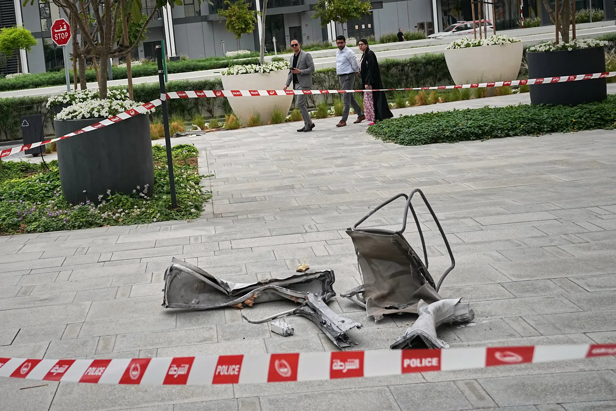 Okoloidúci sa pozerajú na trosky ležiace na chodníku pri hoteli Address Creek Harbour po tom, ako ho zasiahol iránsky dron v Dubaji.