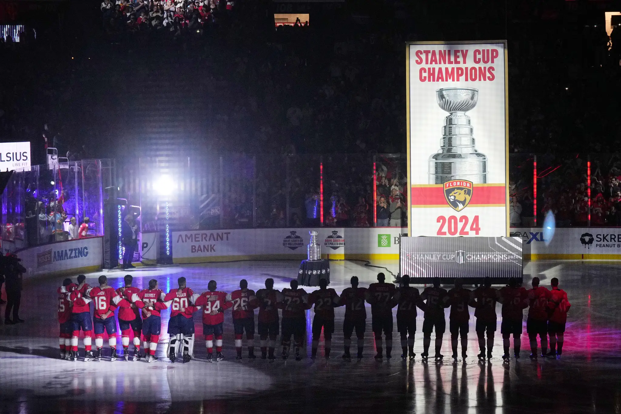 Obhajcovia Stanleyho pohára hokejisti Floridy Panthers stoja pri vztýčenej klubovej vlajke.