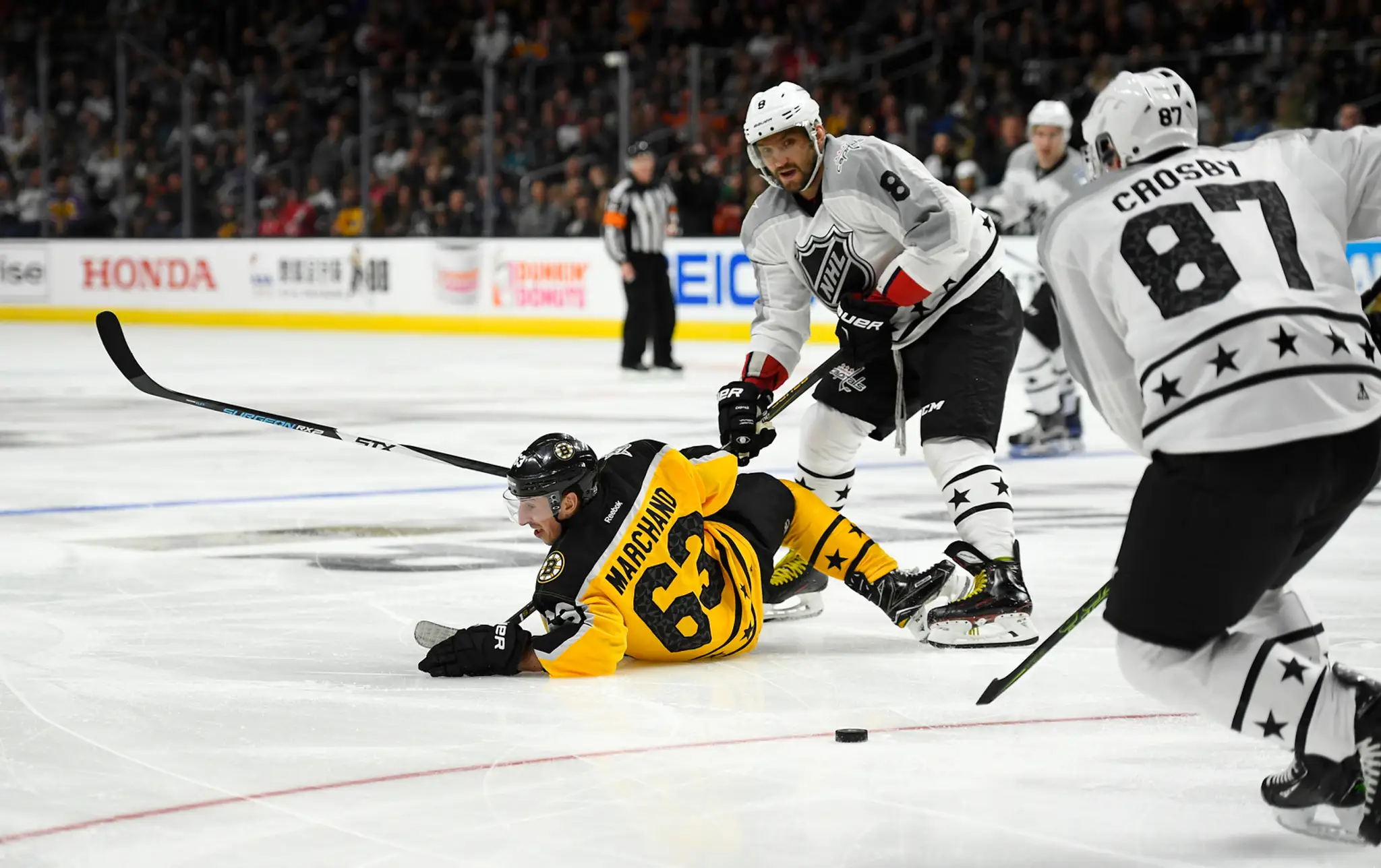 Útočník Atlantickej divízie Brad Marchand leží na ľade po strete s Alexandrom Ovečkinom, Sidney Crosby s pukom (vpravo).