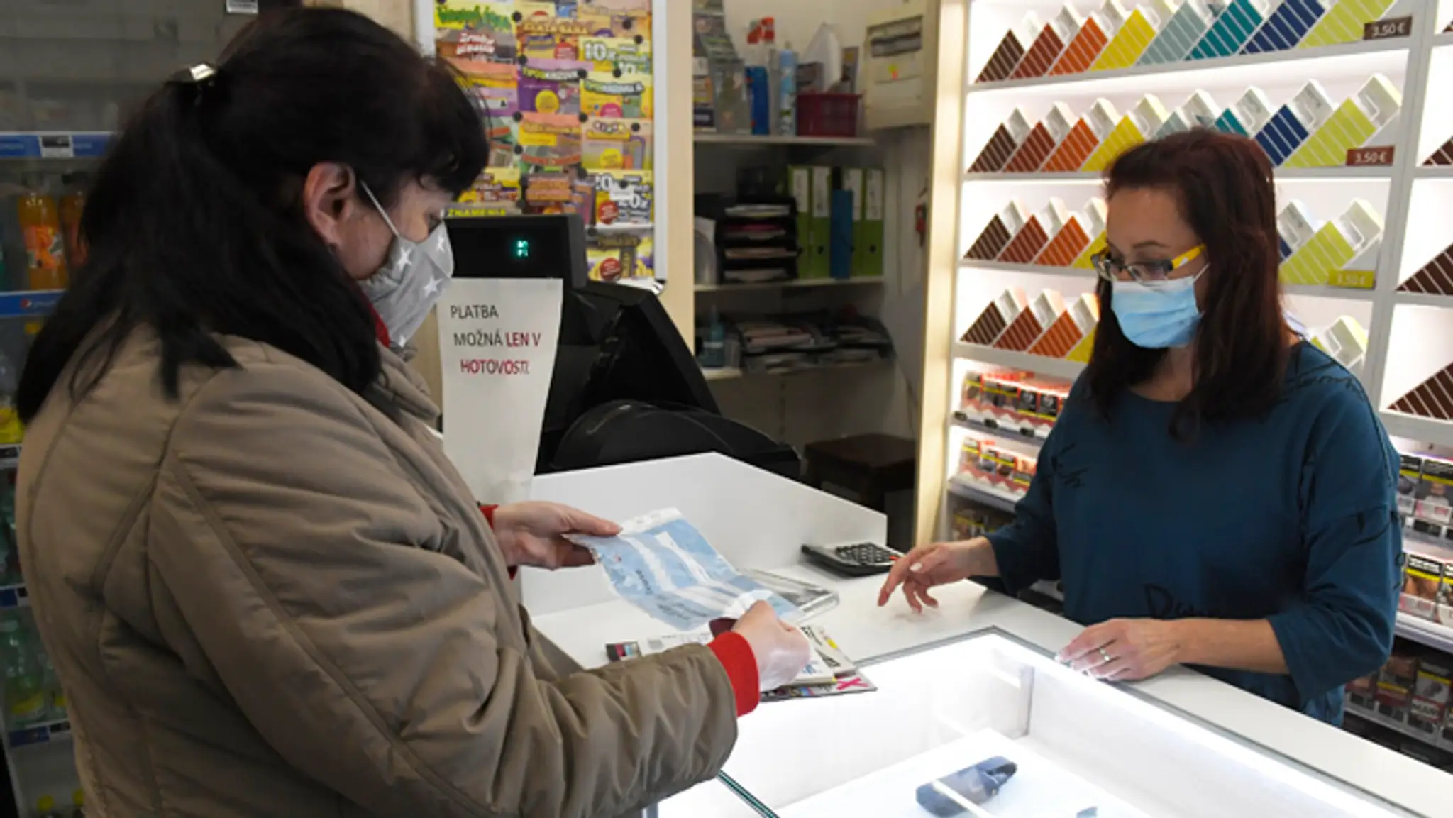 Predavačka v predajni tabaku kontroluje antigénový certifikát o testovaní na COVID-19.