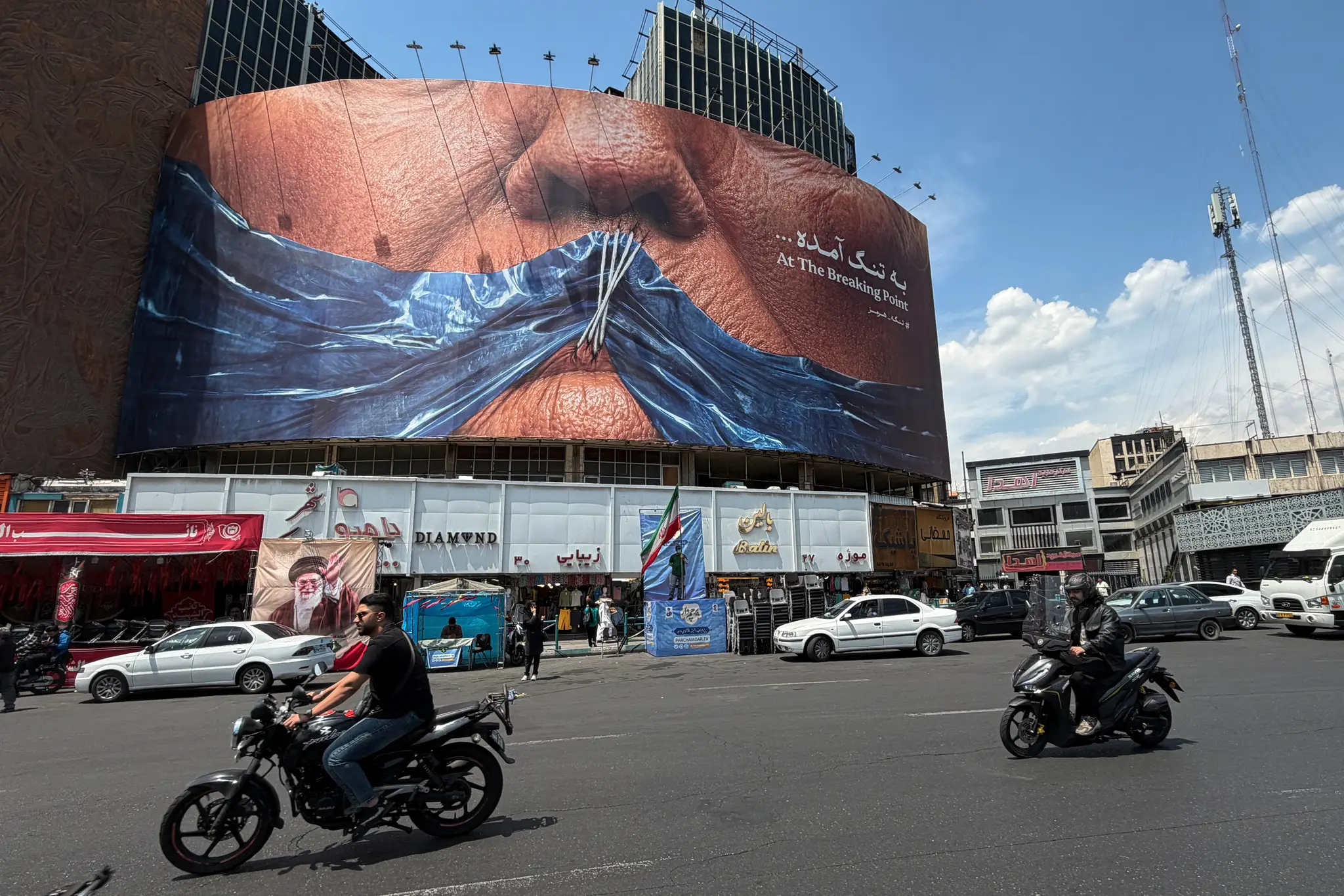 Na námestí v Teheráne prechádzajú autá okolo billboardu s obrázkom Hormuzského prielivu a zošitými perami Donalda Trumpa.