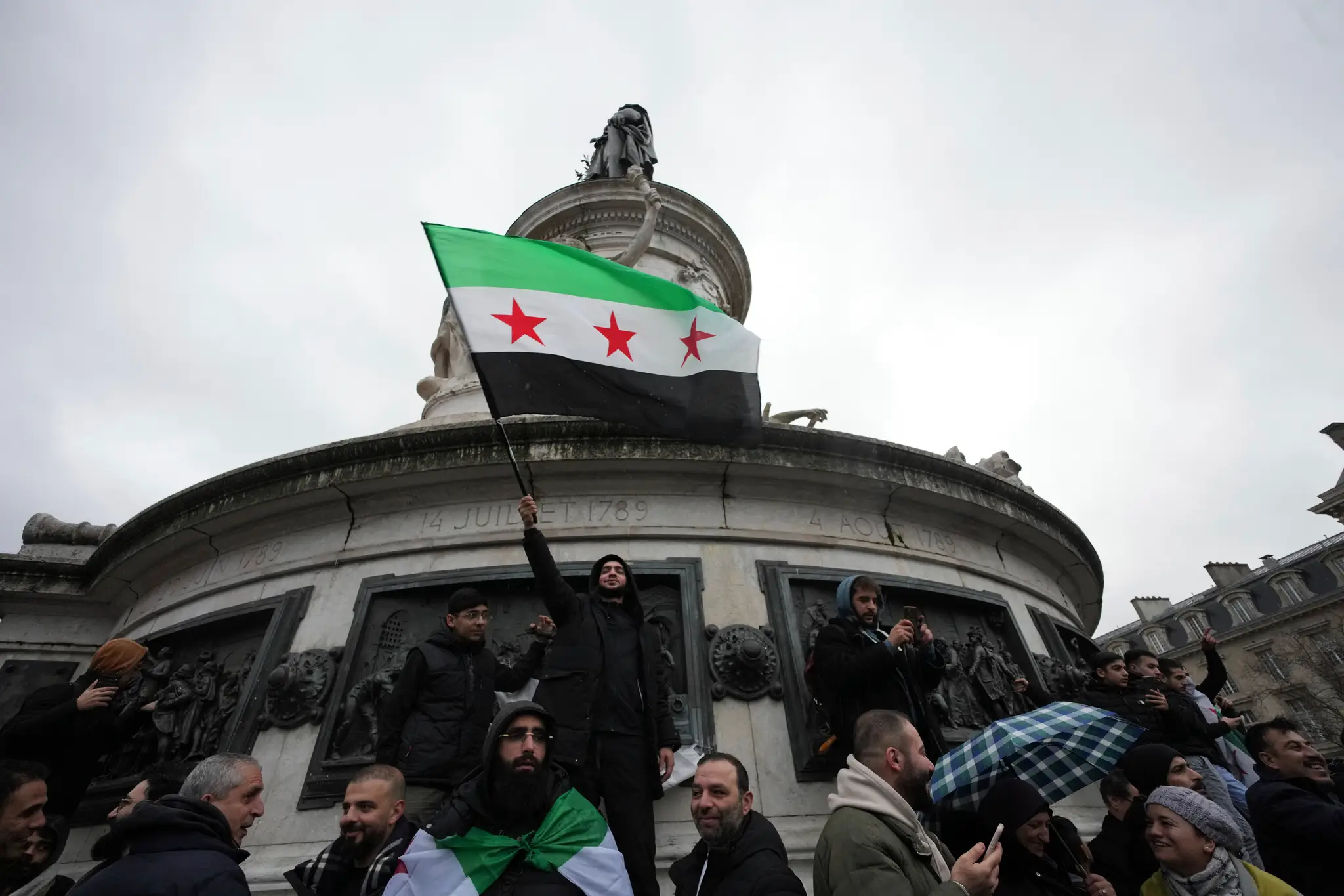 Sýrčania žijúci vo Francúzsku mávajú národnou zástavou počas zhromaždenia na Námestí republiky po páde sýrskeho vládneho režimu v Paríži.