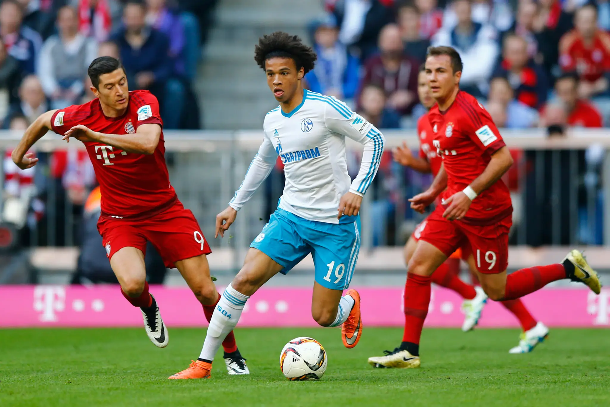 Hráč Schalke Leroy Sane v súboji o loptu s hráčmi Bayernu Robertom Lewandowskim a Máriom Götzem.