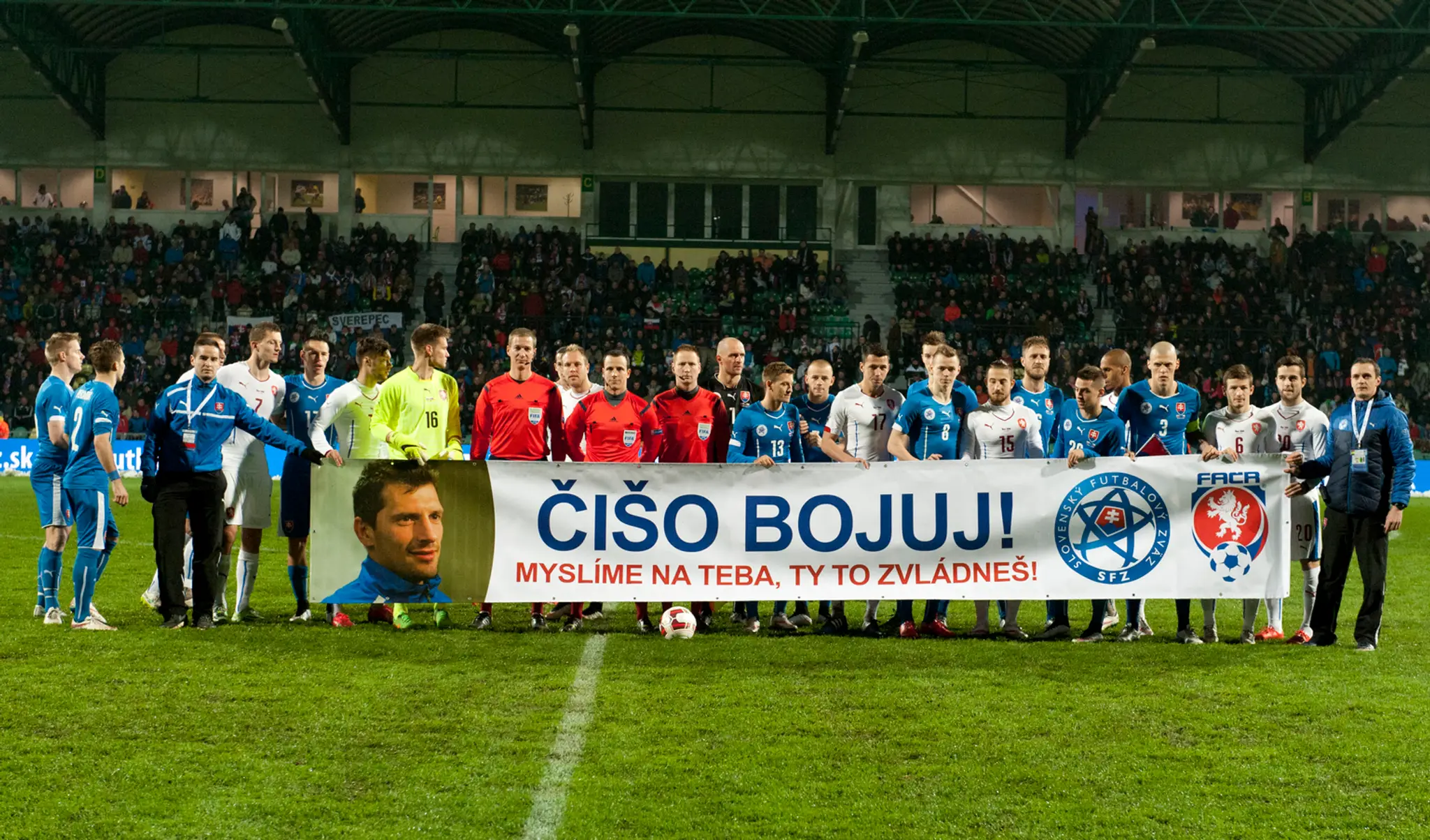 Hráči oboch tímov s transparentom na podporu svojho chorého kolegu.