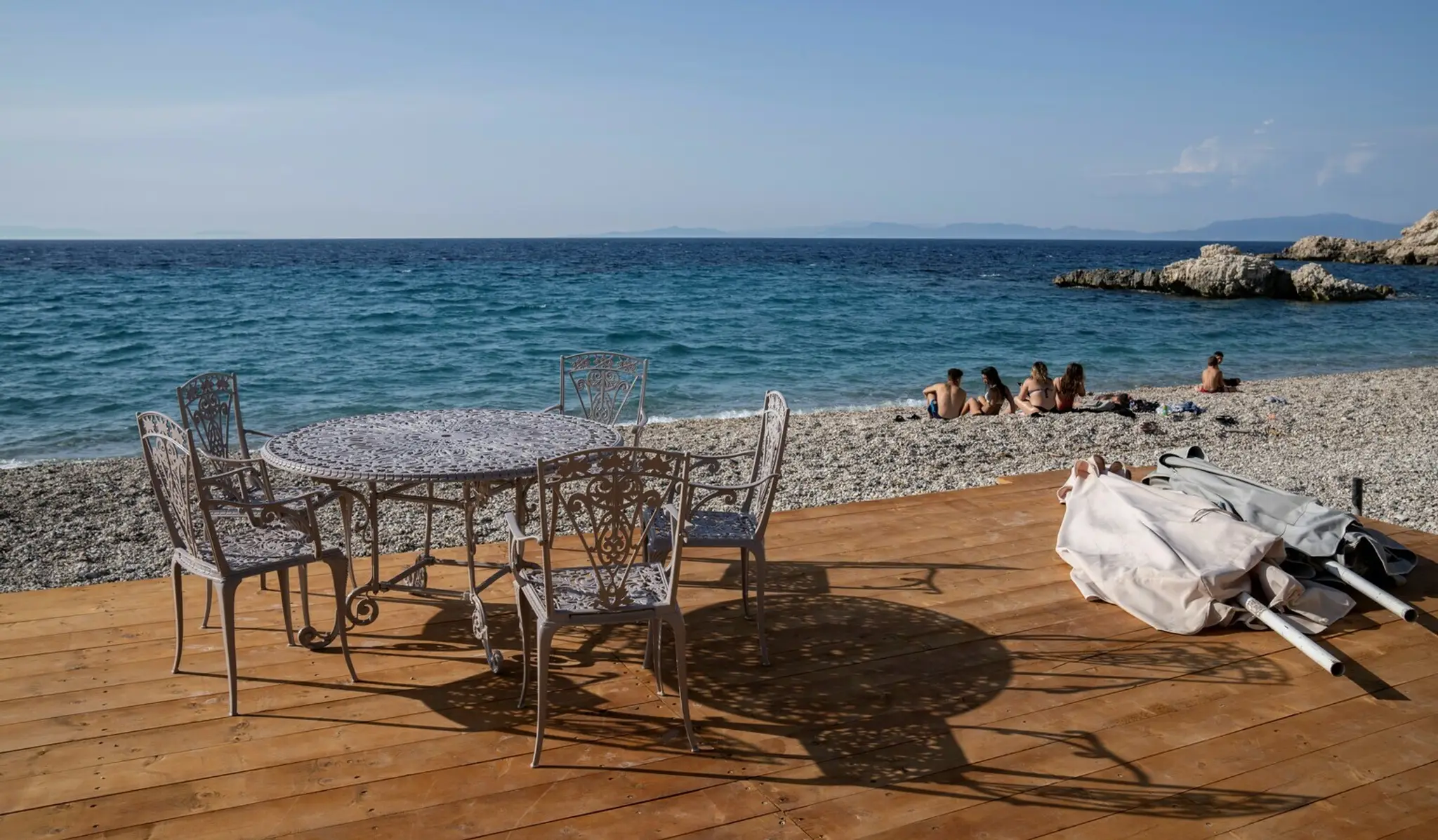 Ľudia sedia na pláži pred tavernou v meste Kokkari na gréckom ostrove Samos.