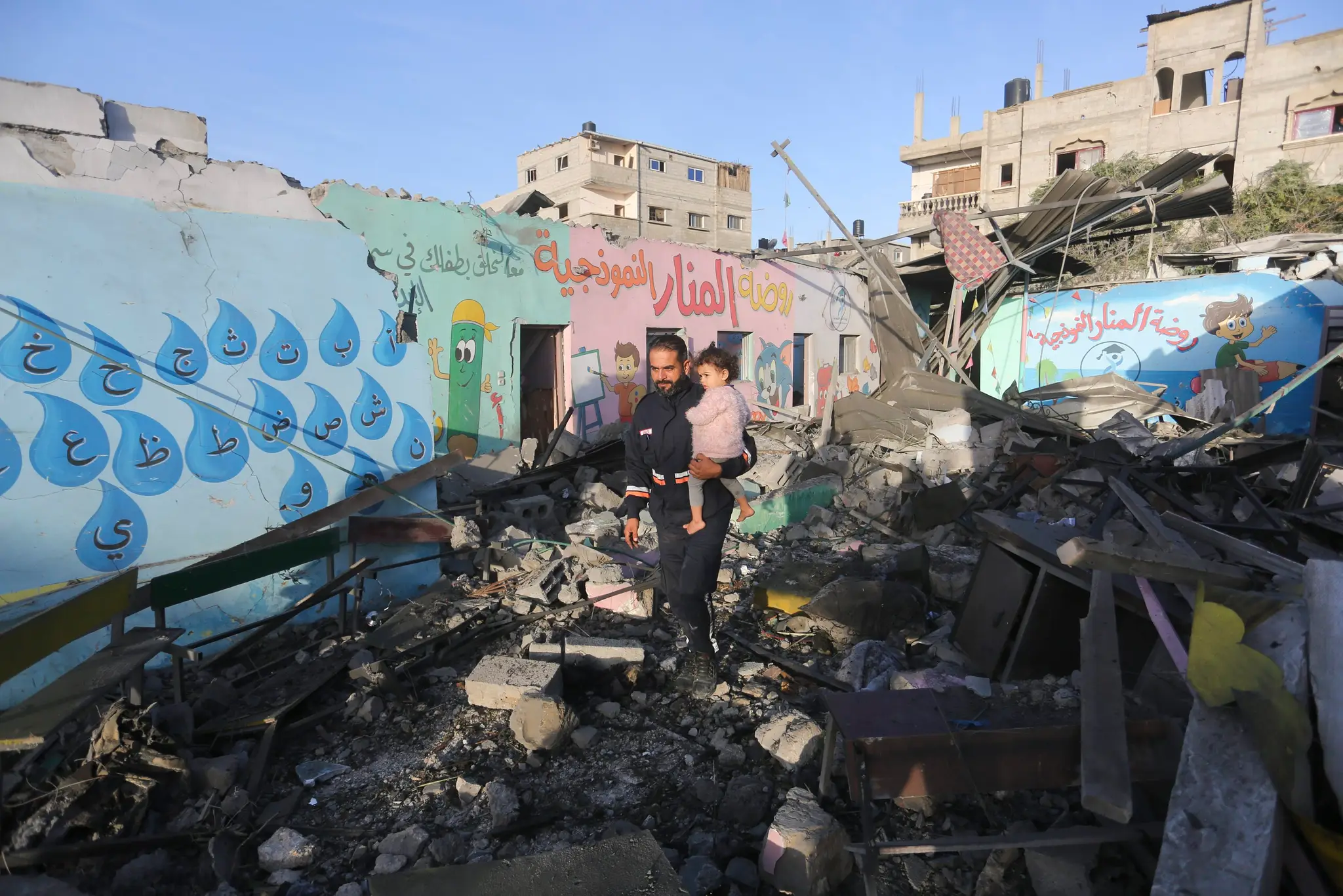 Palestínčania kráčajú okolo budovy zničenej izraelským bombardovaním v noci v Rafahu.