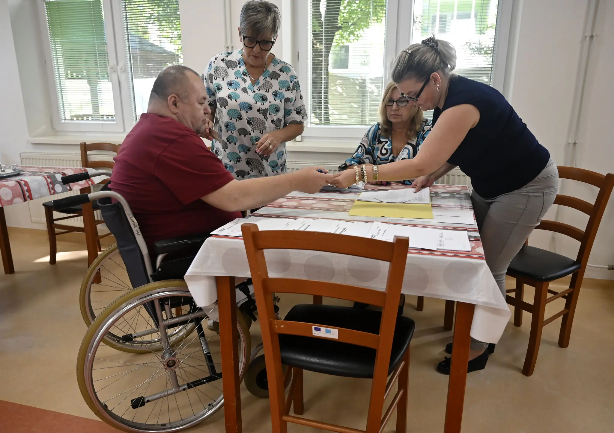 Členovia volebnej okrskovej komisie s prenosnou volebnou schránkou overujú totožnosť voliča v zariadení opatrovateľskej služby Prameň nádeje v Trebišove.