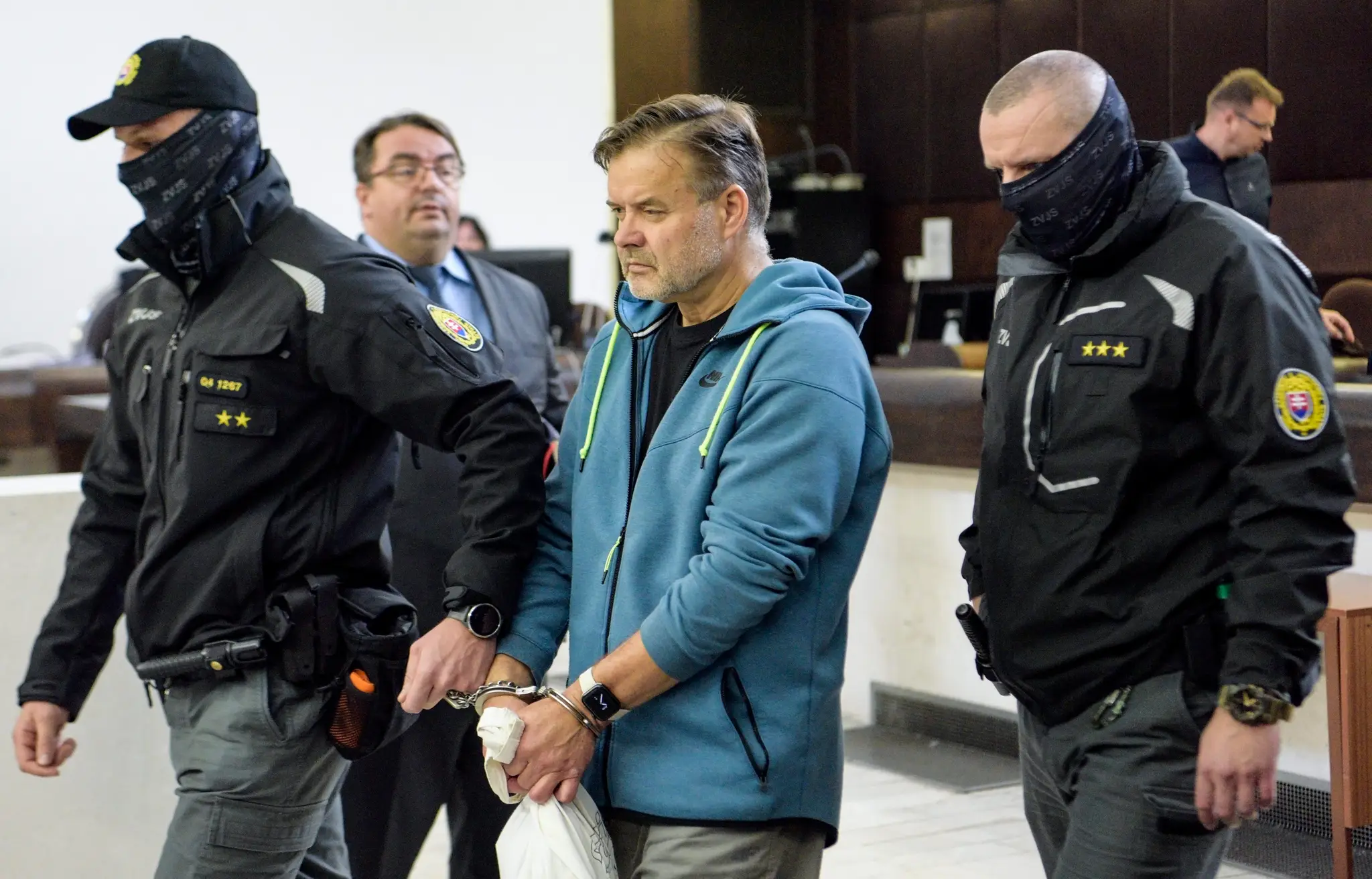 Obvineného Dušana Dědečka odvádzajú členovia Zboru väzenskej a justičnej stráže do väzby (14. októbra 2022). 