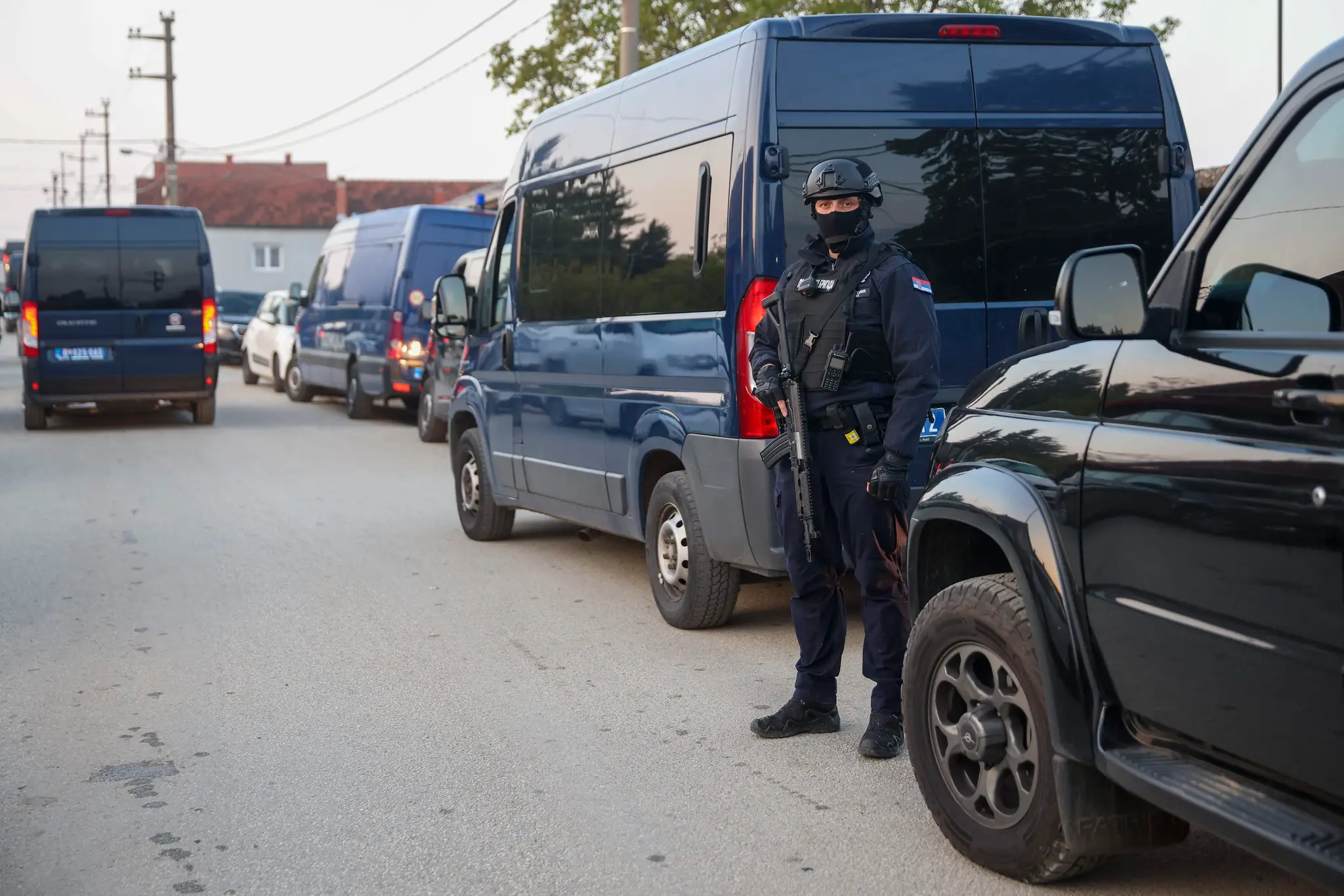 Policajt stojí pri policajnom aute so zbraňou v ruke.
