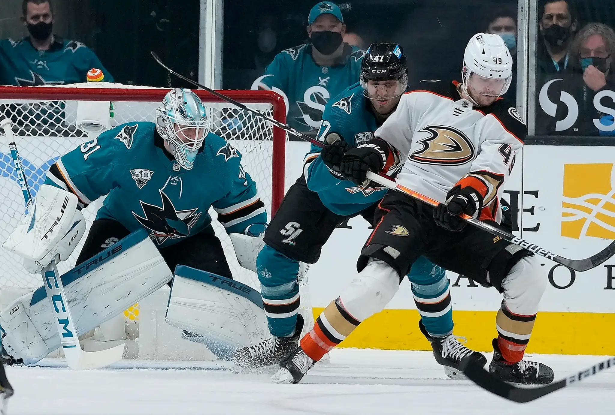 Na snímke uprostred slovenský obranca Sharks Christián Jaroš, vpravo útočník Ducks Max Jones a vľavo brankár Martin Jones.