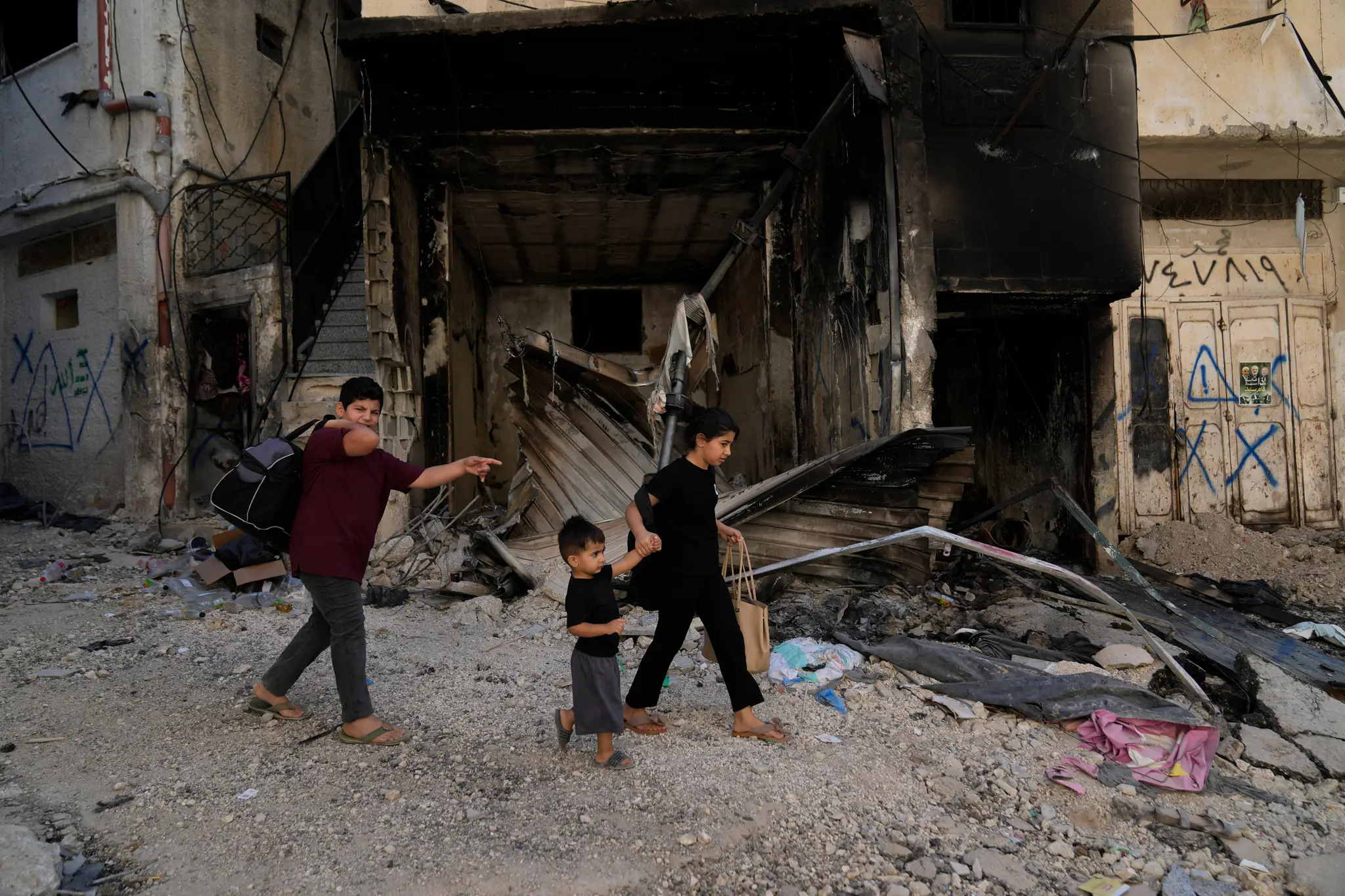 Palestínski utečenci kráčajú okolo zhoreného domu.