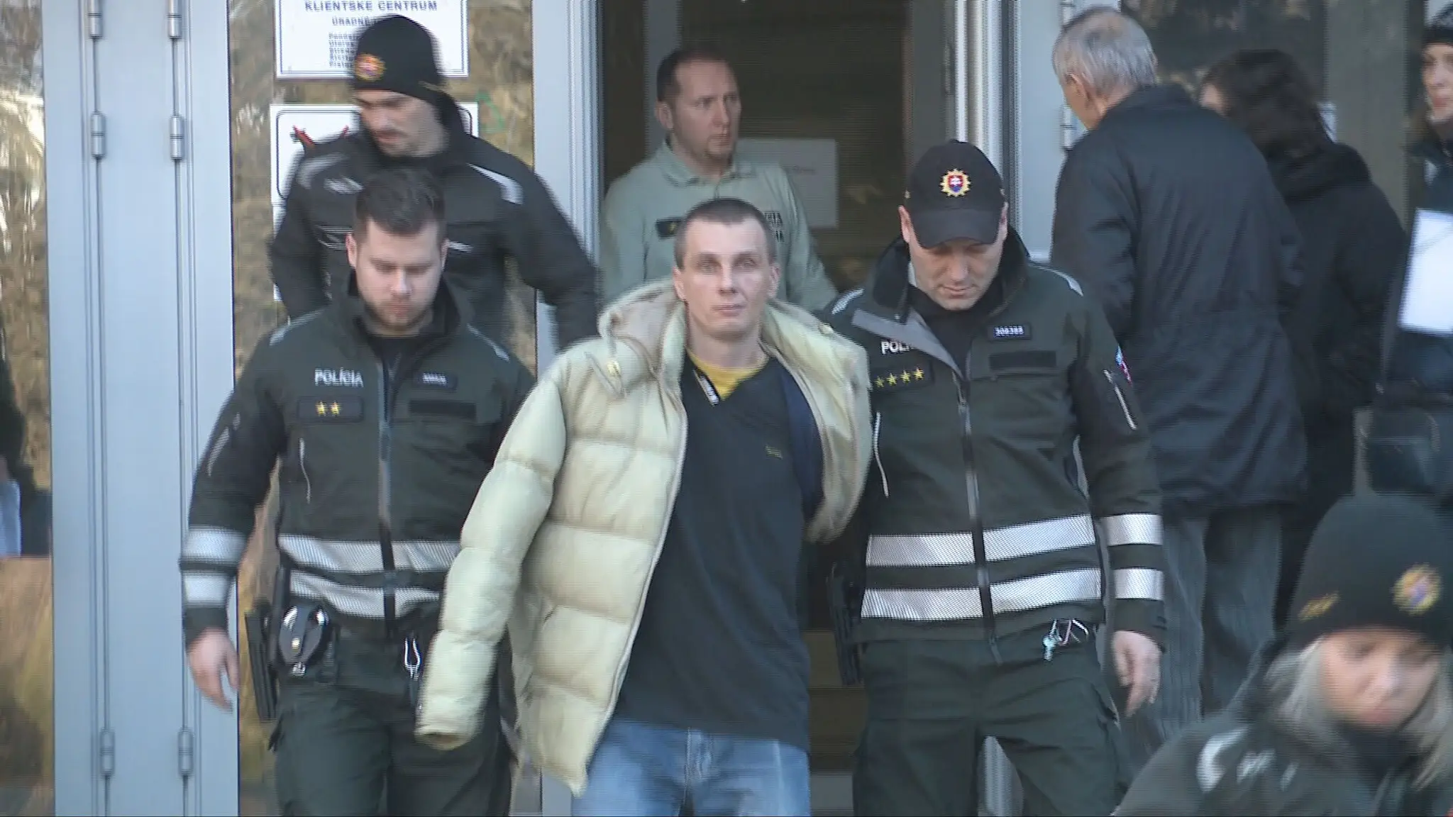 Polícia odvádza muža, ktorý spustil bombový poplach v klientskom centre.
