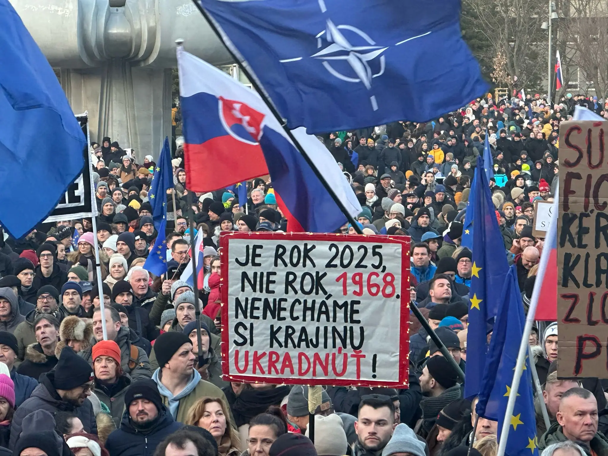 Protestujúci s nápismi a vlajkou NATO