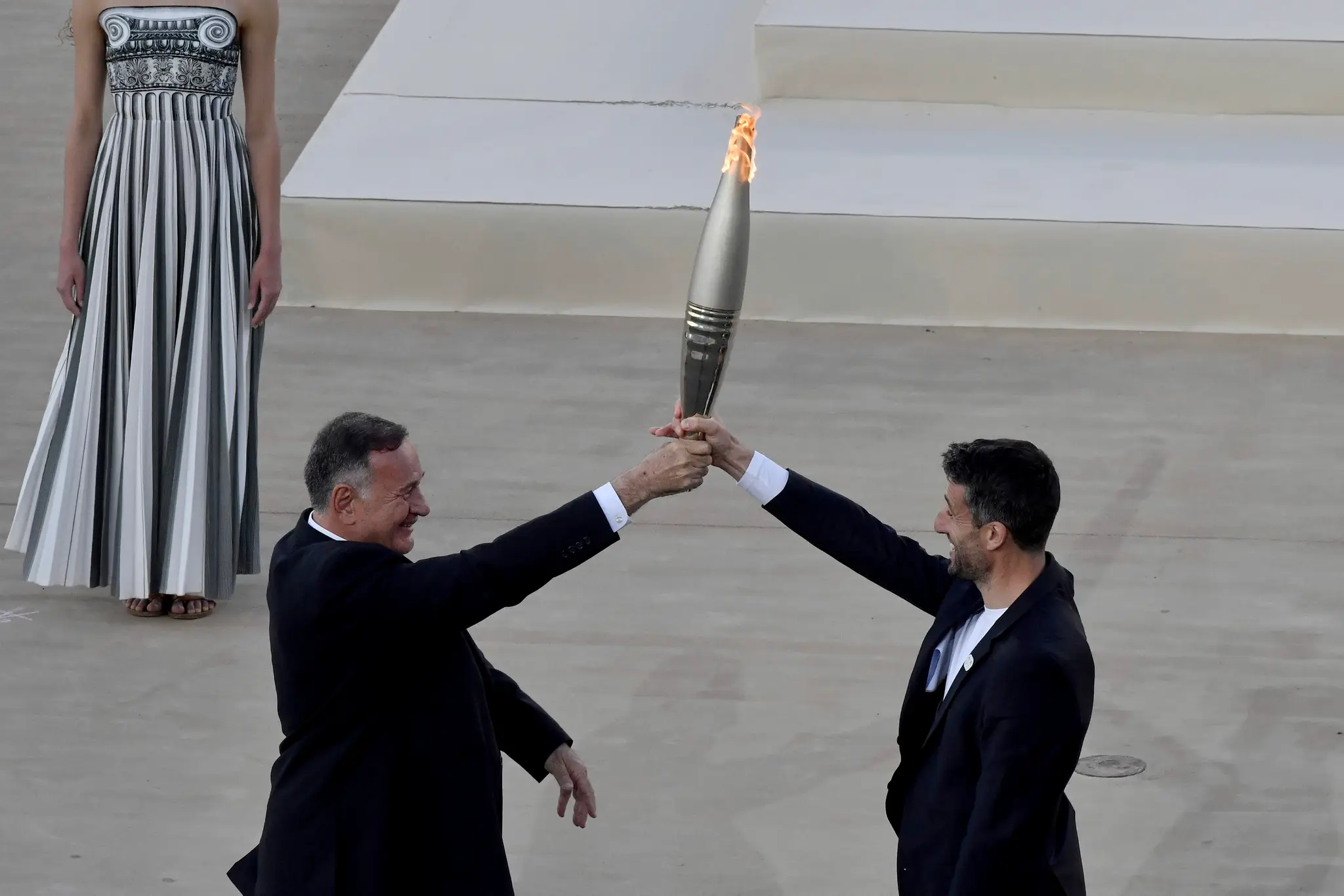 Šéf Gréckeho olympijského výboru Spyros Capralos (vľavo) odovzdáva olympijský oheň predsedovi francúzskeho organizačného výboru Tonymu Estanguetovi.
