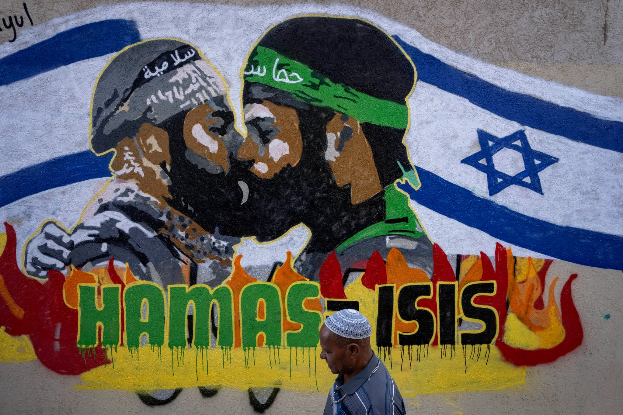 Muž kráča okolo grafitu s nápisom Hamas rovná sa Islamský štát v Tel Avive.