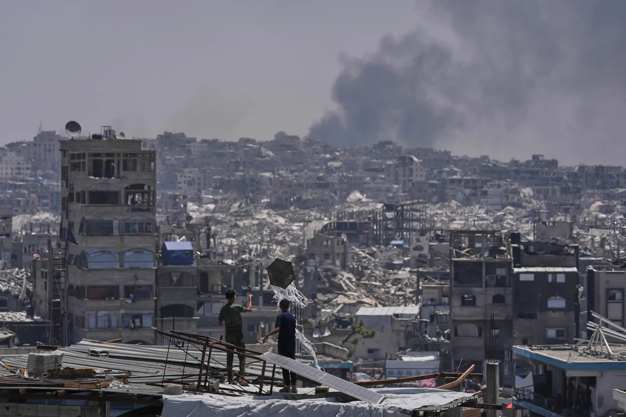 Palestínčania sa pozerajú ako dym stúpa pri explózii po izraelskom bombardovaní Pásma Gazy.
