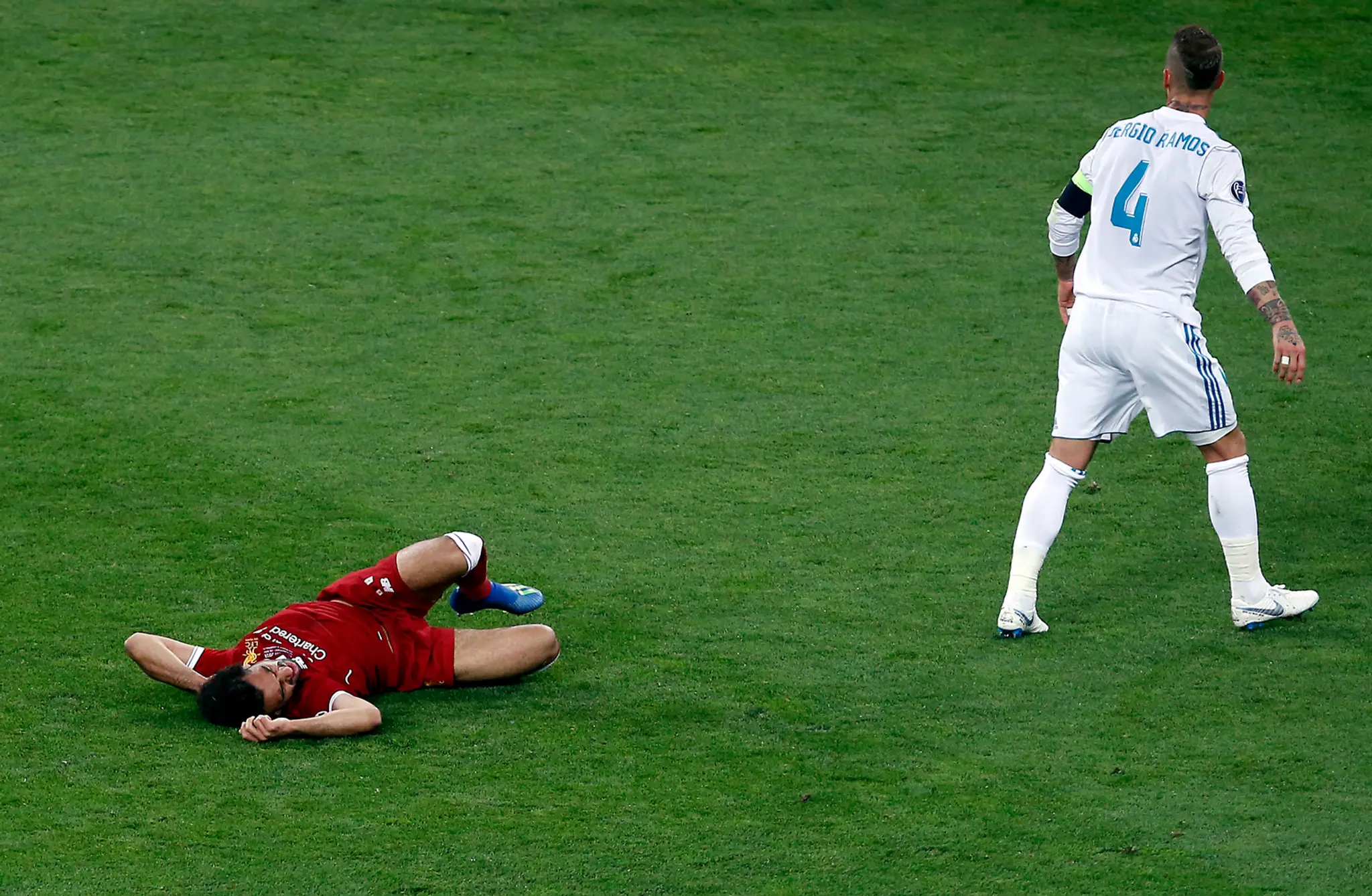 Salah leží v bolestiach na trávniku po zrážke s Ramosom.