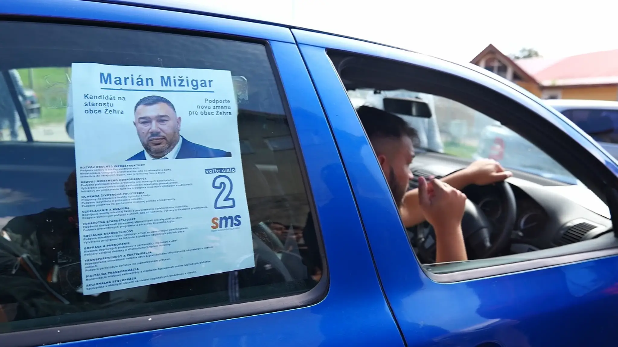 Miestni s plagátom s podobizňou kandidáta.