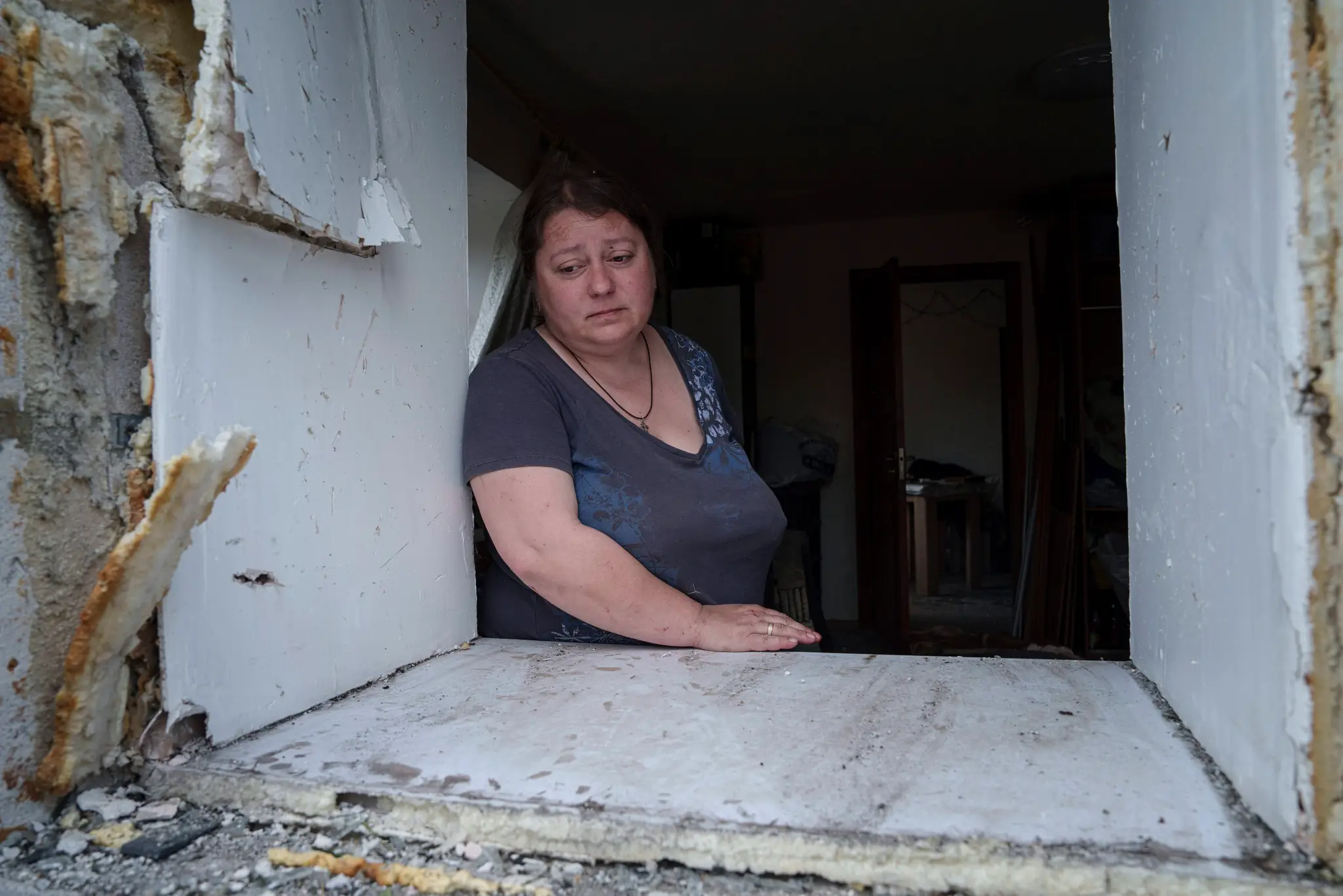 Žena sa pozerá cez okno svojho poškodeného domu po ruskom nálete na obytnú štvrť v Charkove.