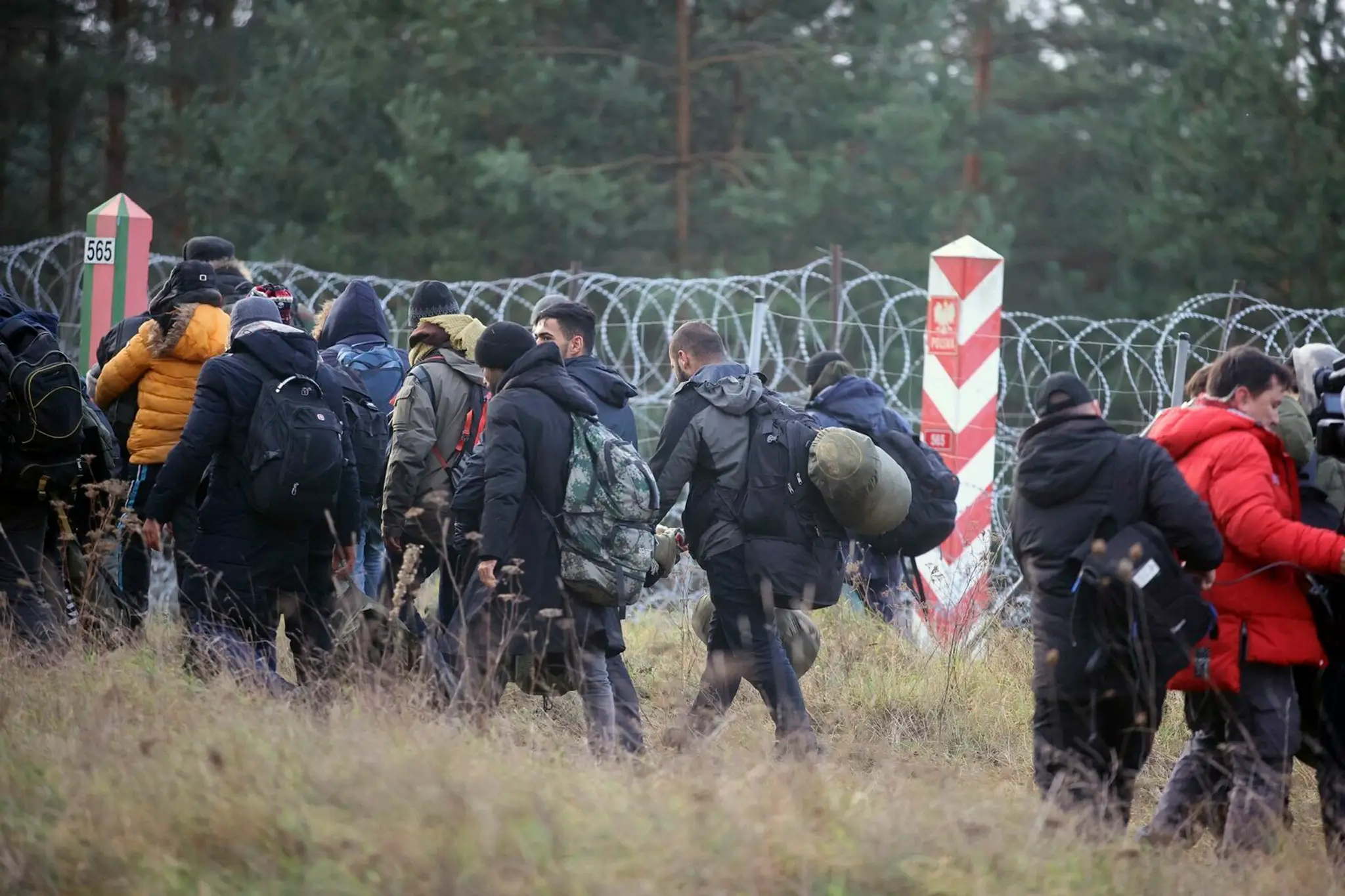 Migranti z Blízkeho východu a iných krajín kráčajú pozdĺž oplotenia s ostnatým drôtom na hranici pri bieloruskej dedine Grodno.