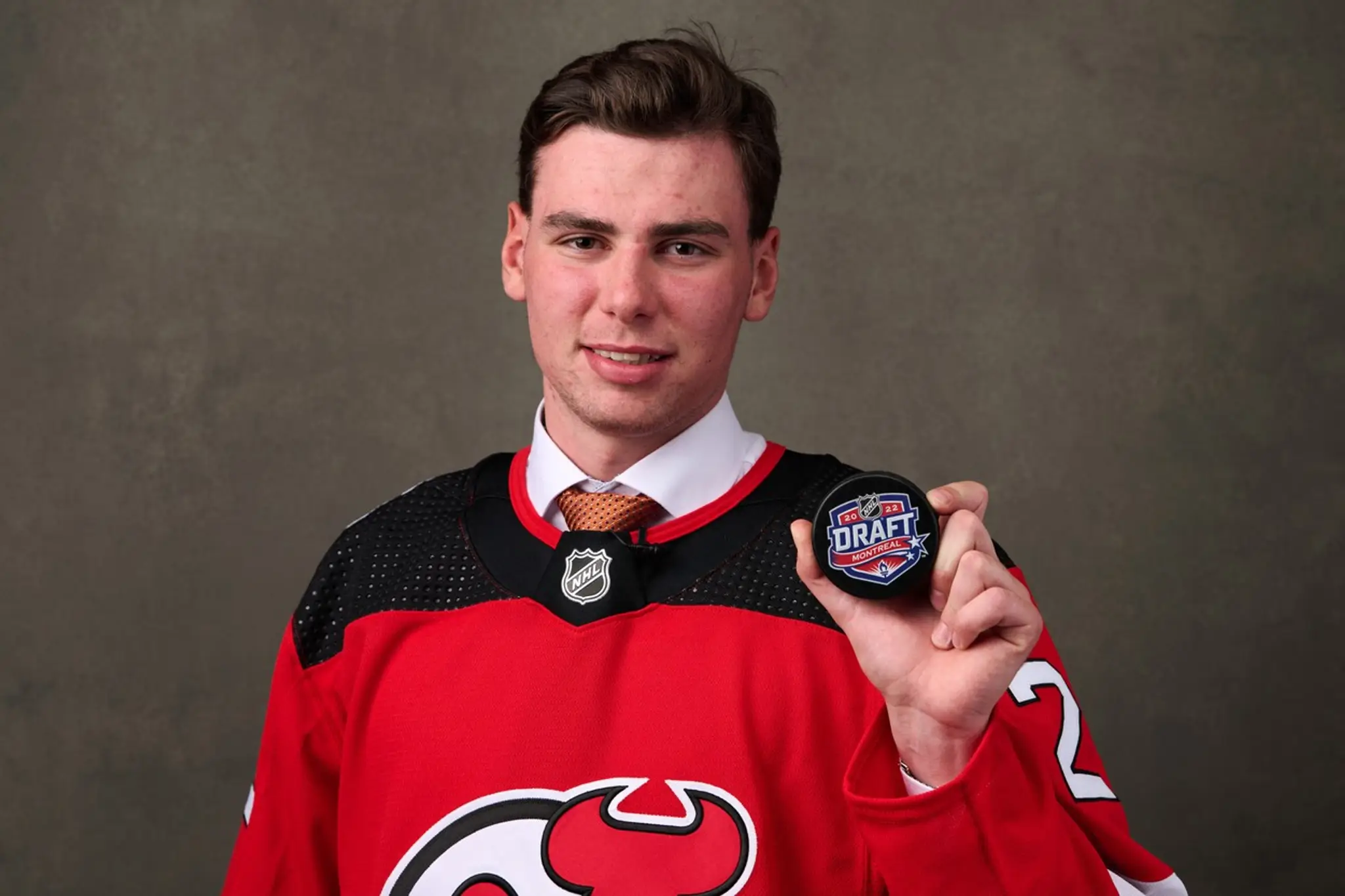 Šimon Nemec pózuje s pukom v drese New Jersey, ktoré si ho vybralo ako dvojku v drafte NHL 2022.