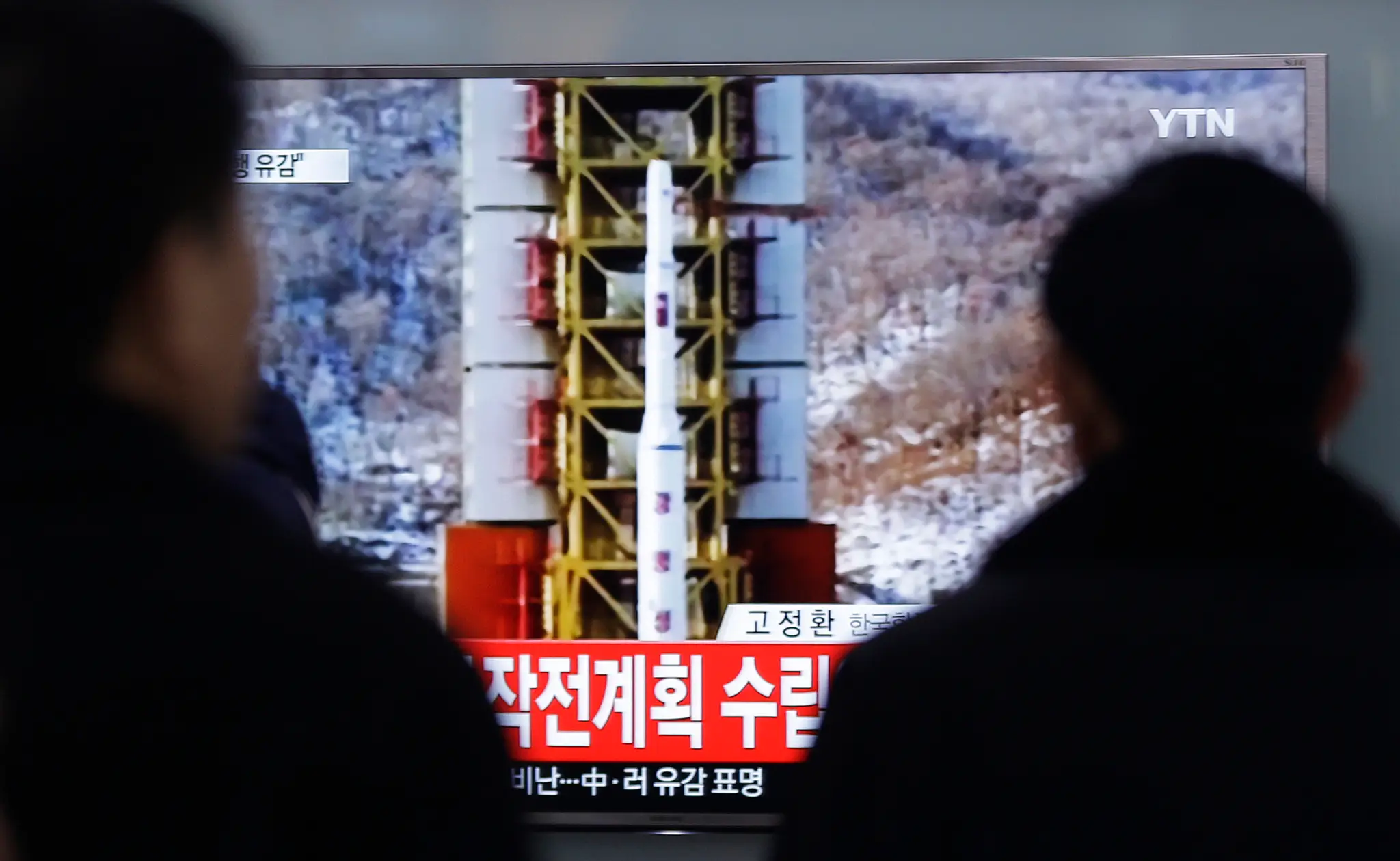  Ľudia sledujú televízne spravodajstvo o vypustení rakety dlhého doletu.