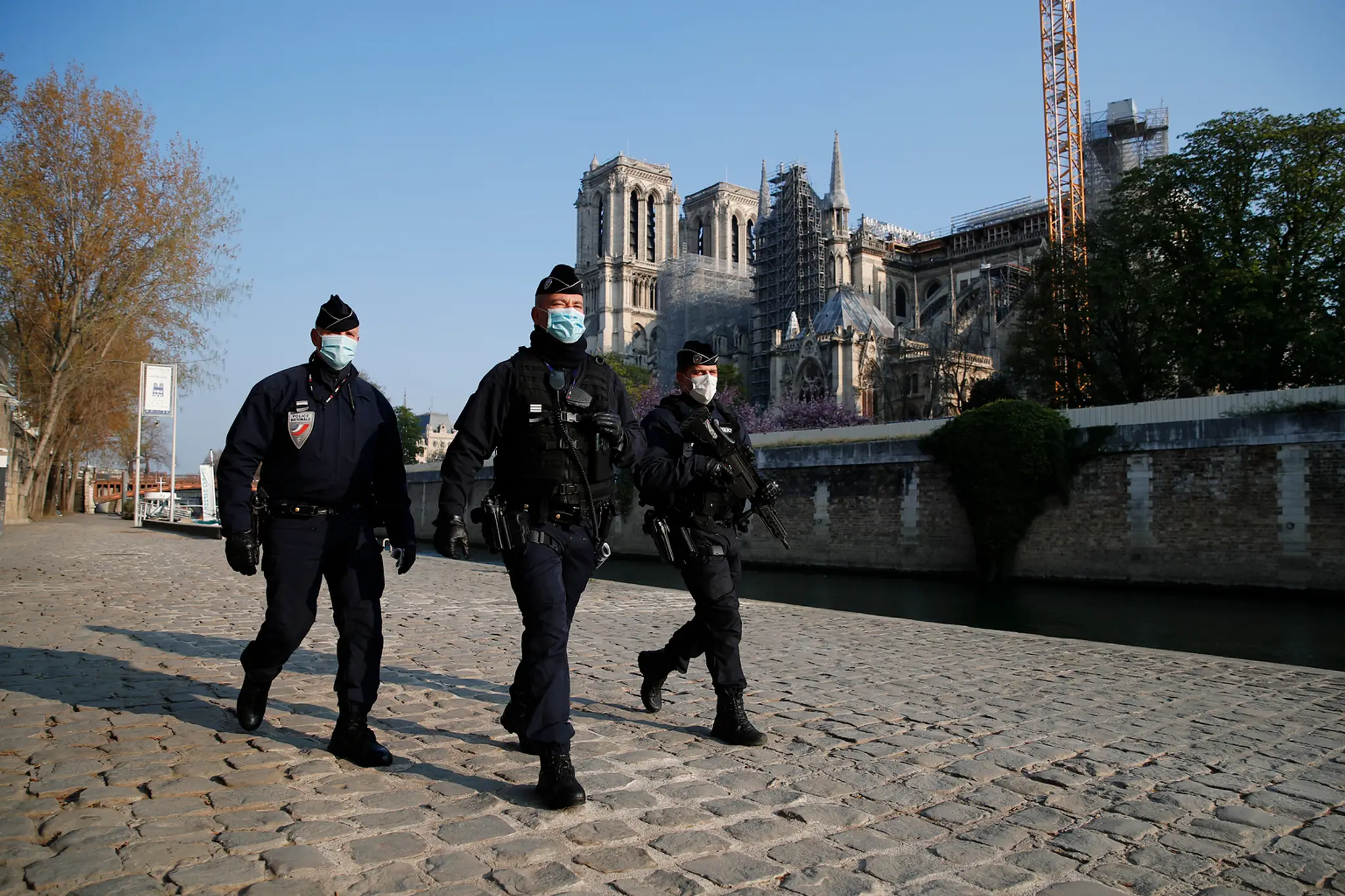 Policajti hliadkujú pozdĺž rieky Seiny, v pozadí katedrála Notre-Dame počas druhého výročia ničivého požiaru.