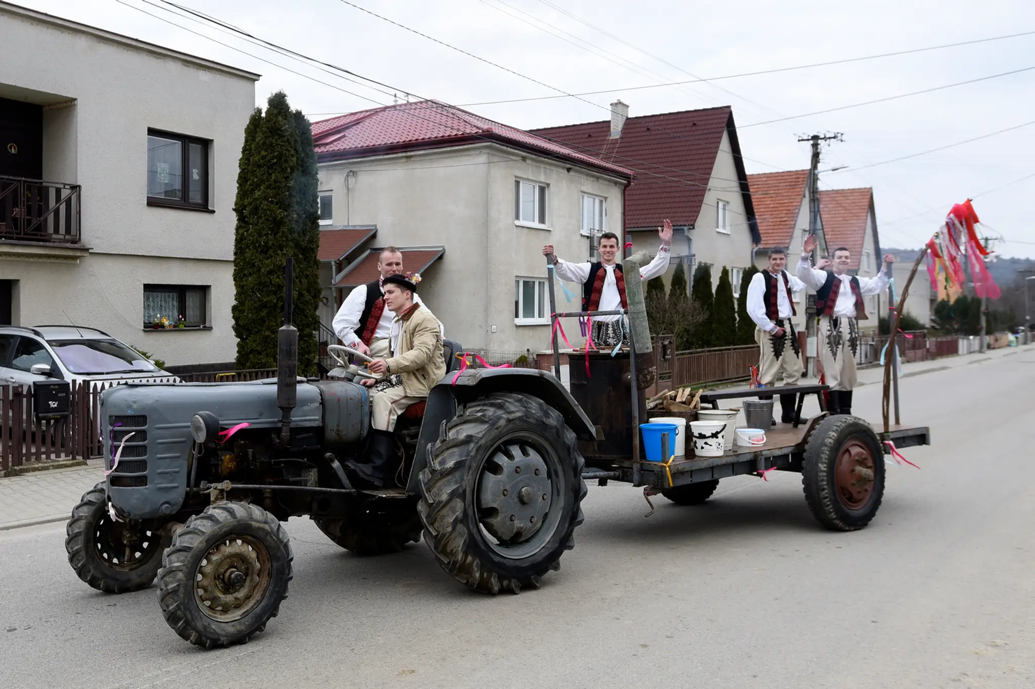 Mládenci v ľudových krojoch na vlečke za traktorom sa presúvajú  po obci Selec neďaleko Trenčína počas oblievačky na Veľkončný p