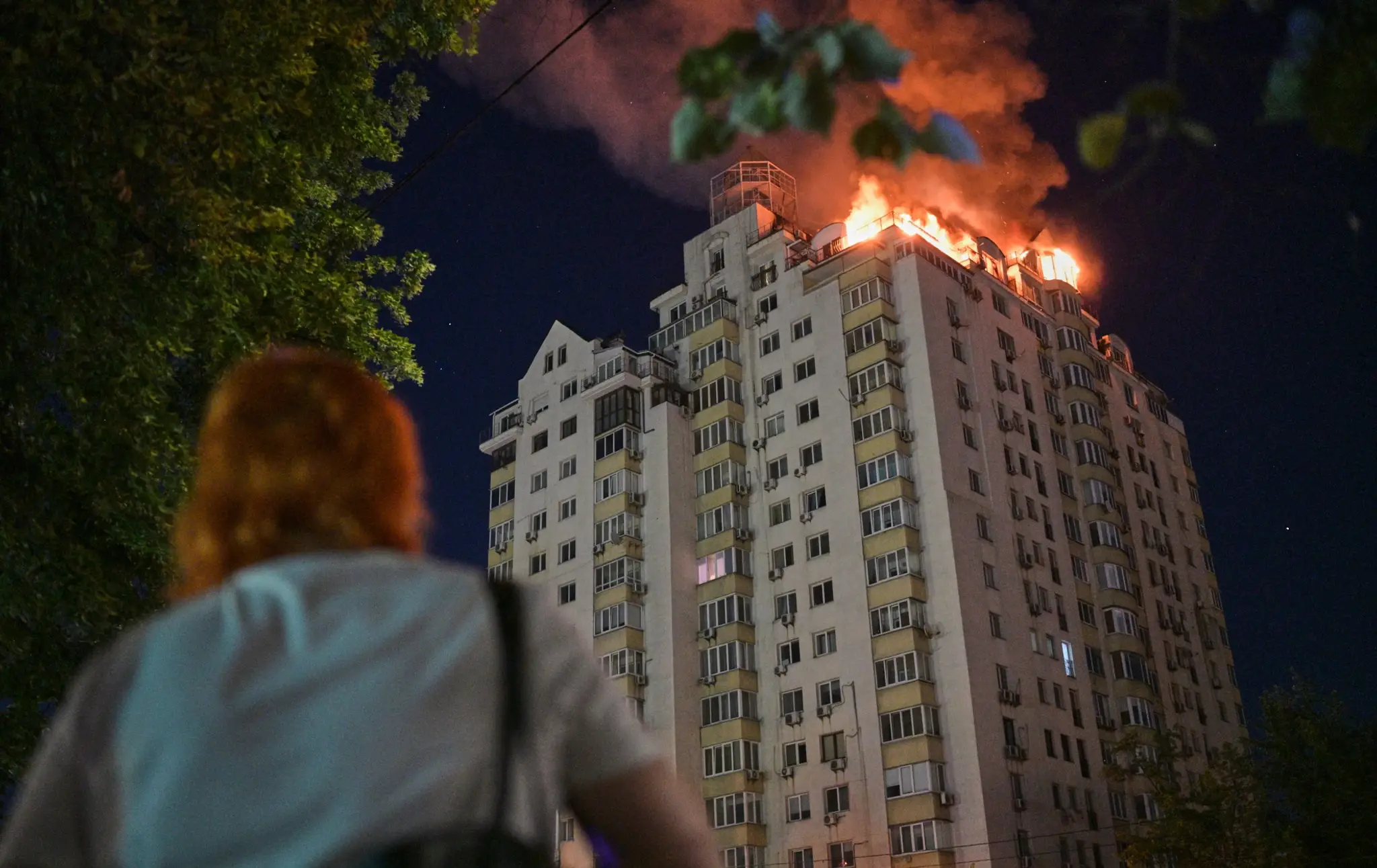 Žena sa pozerá na horiaci bytový dom po ruskom raketovom útoku v Kyjeve.