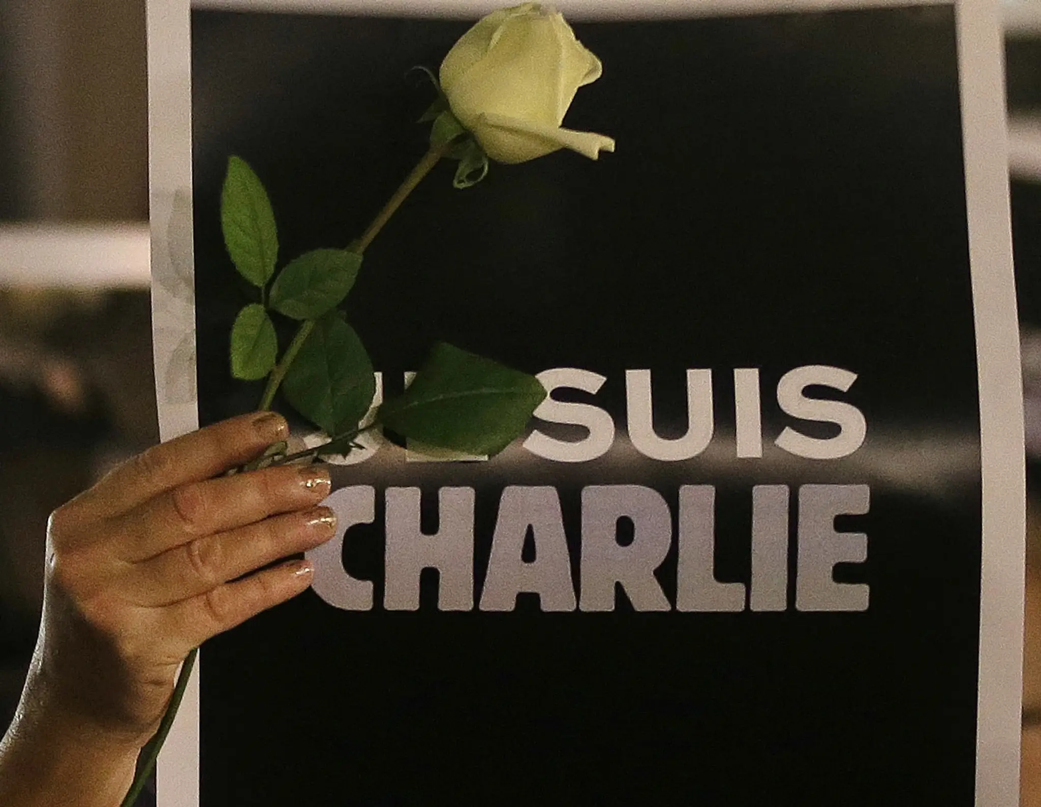 Žena drží plagát s nápisom "Ja som Charlie" a ružu pri spomienke na Charlie Hebdo