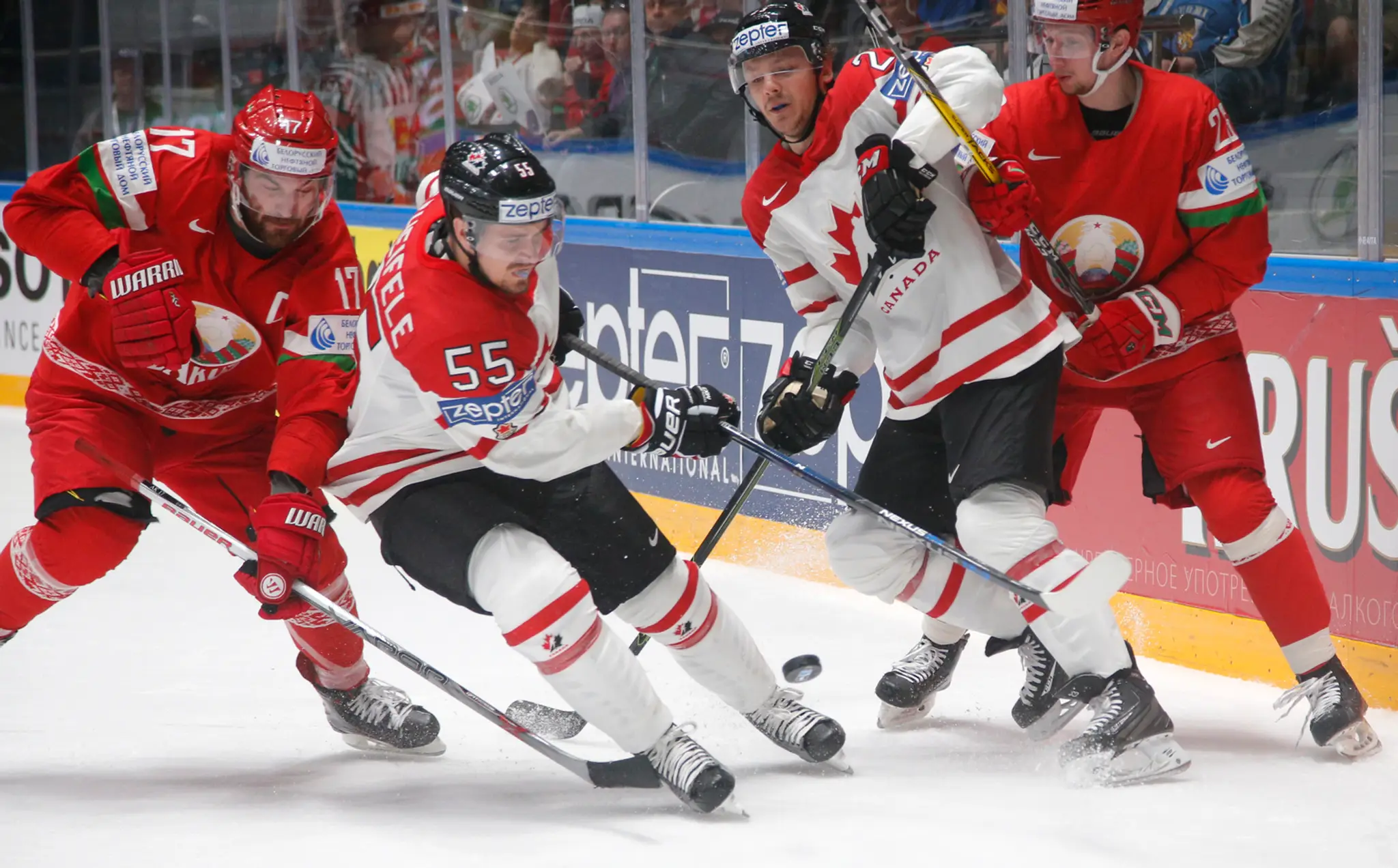 Mark Scheifele (biely vľavo) a Sam Reinhart (biely vpravo) z Kanady v súboji o puk proti dvojicie Bielorusov počas duelu na MS v